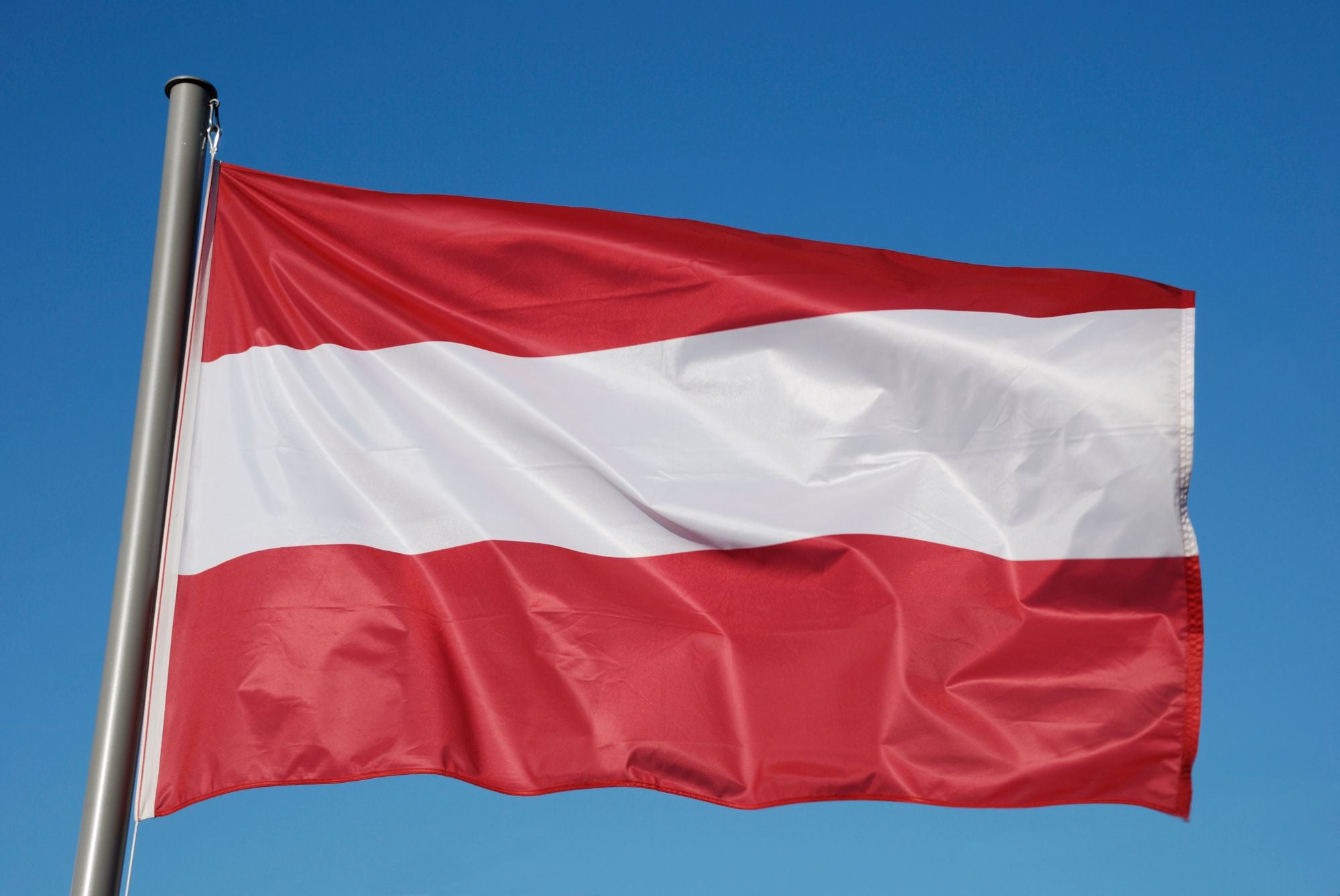 Die österreichische Flagge weht vor klarem, blauem Himmel.