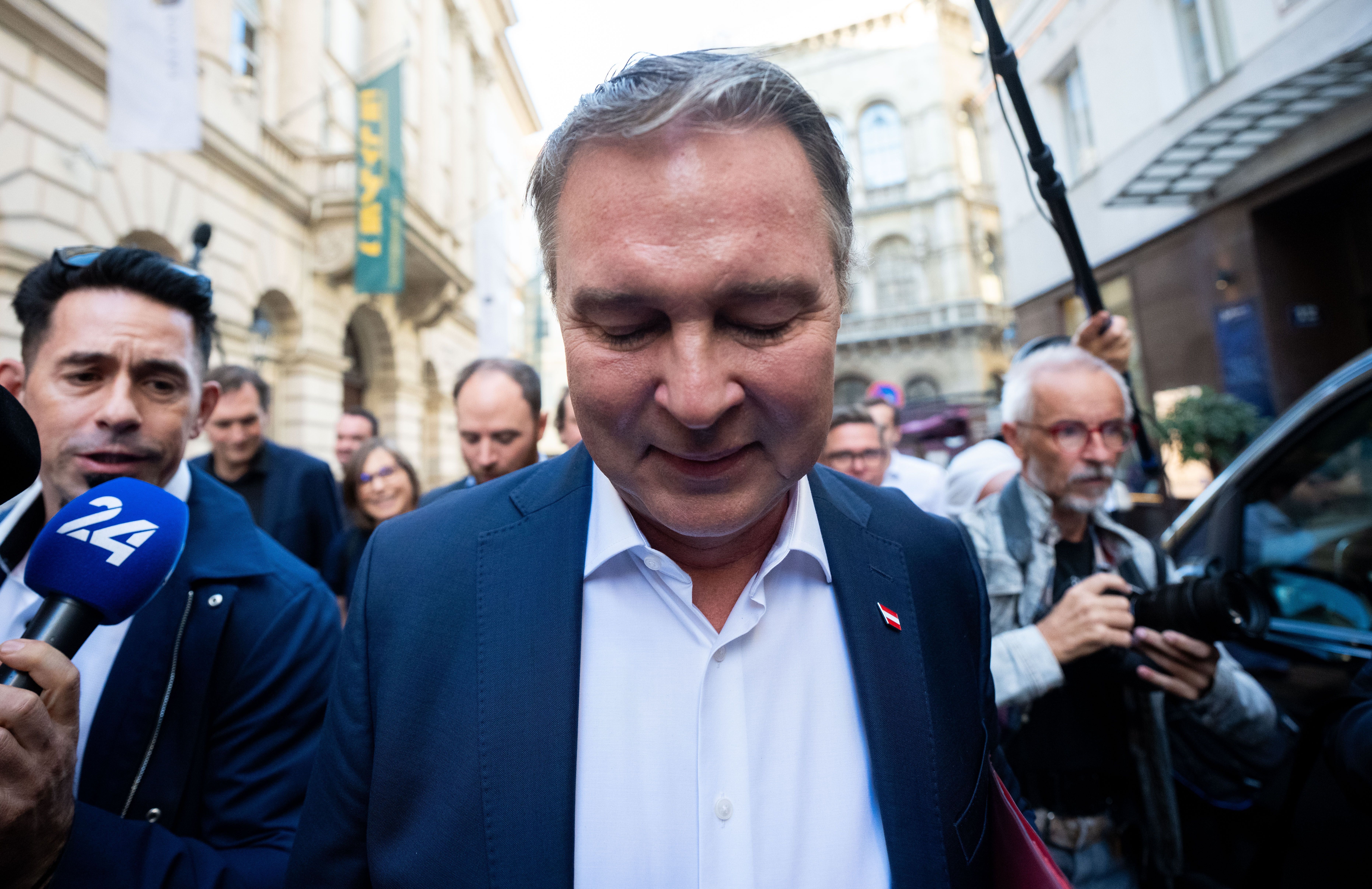 Ein Mann im Anzug ist von Medienvertretern und Fotografen auf einer belebten Straße umgeben.