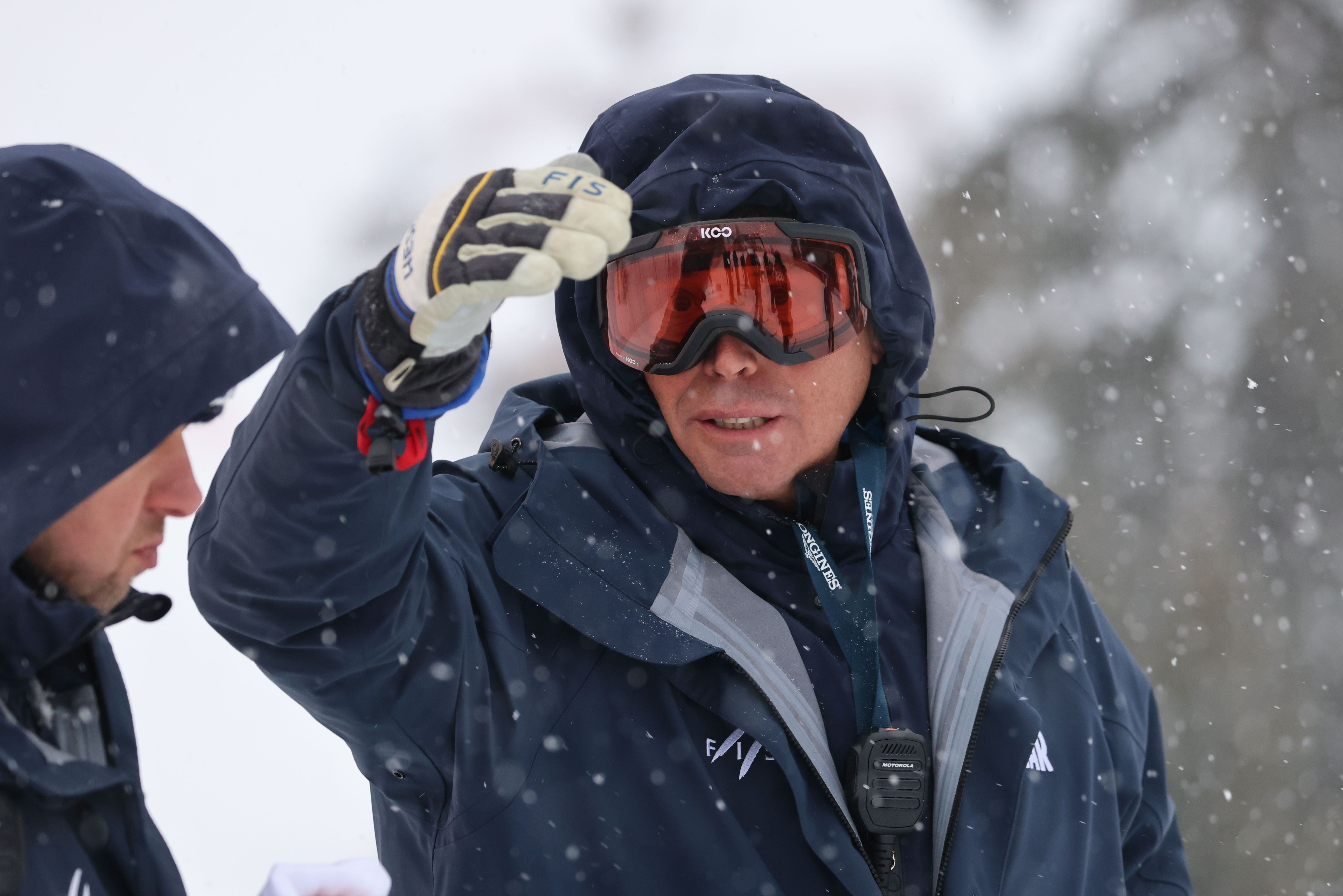 Mann mit Skibrille und Funkgerät spricht im Schneefall mit einer anderen Person.
