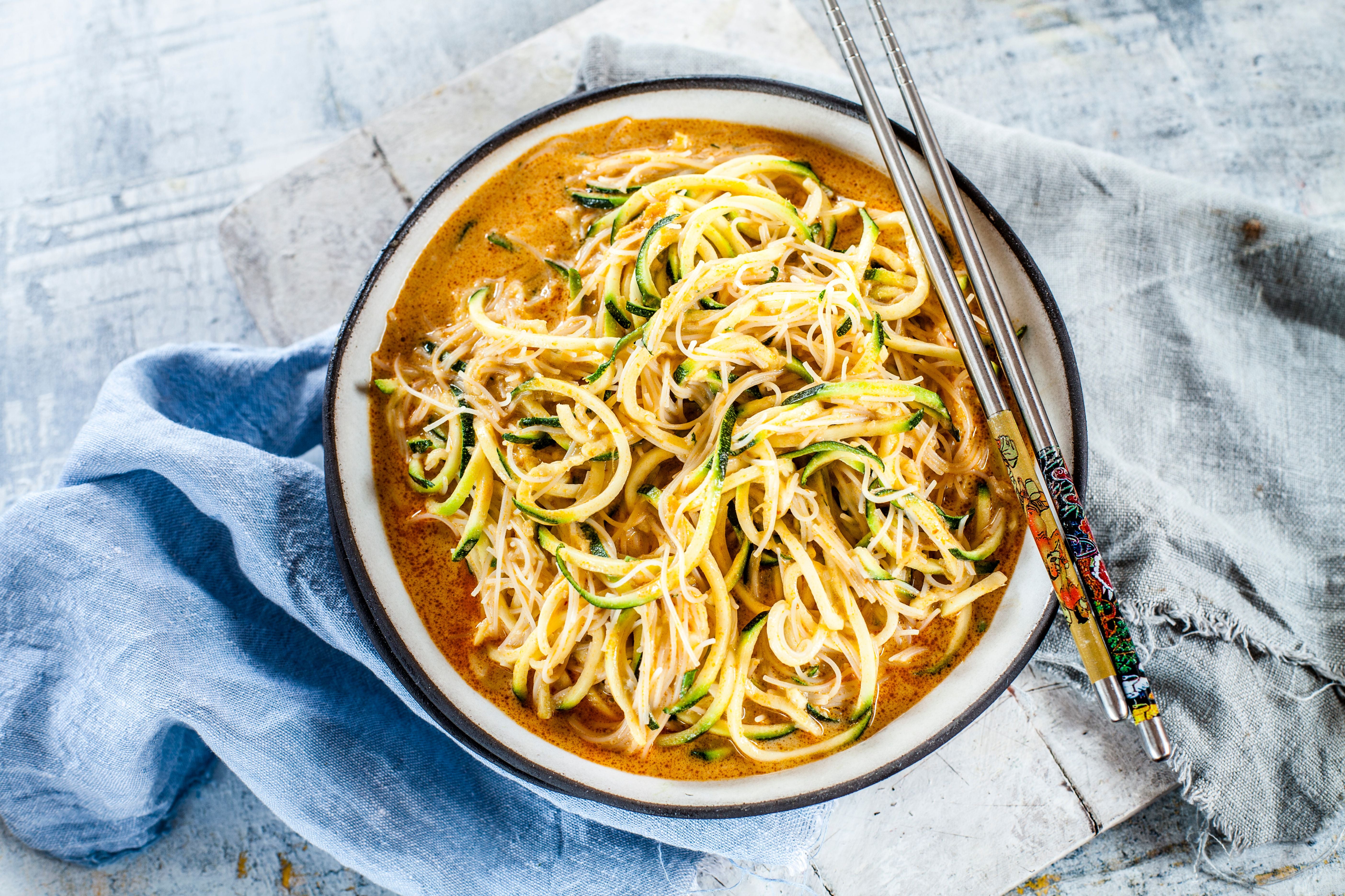Schüssel mit Zucchini-Nudeln in Currysoße, daneben Essstäbchen auf einem Tuch.