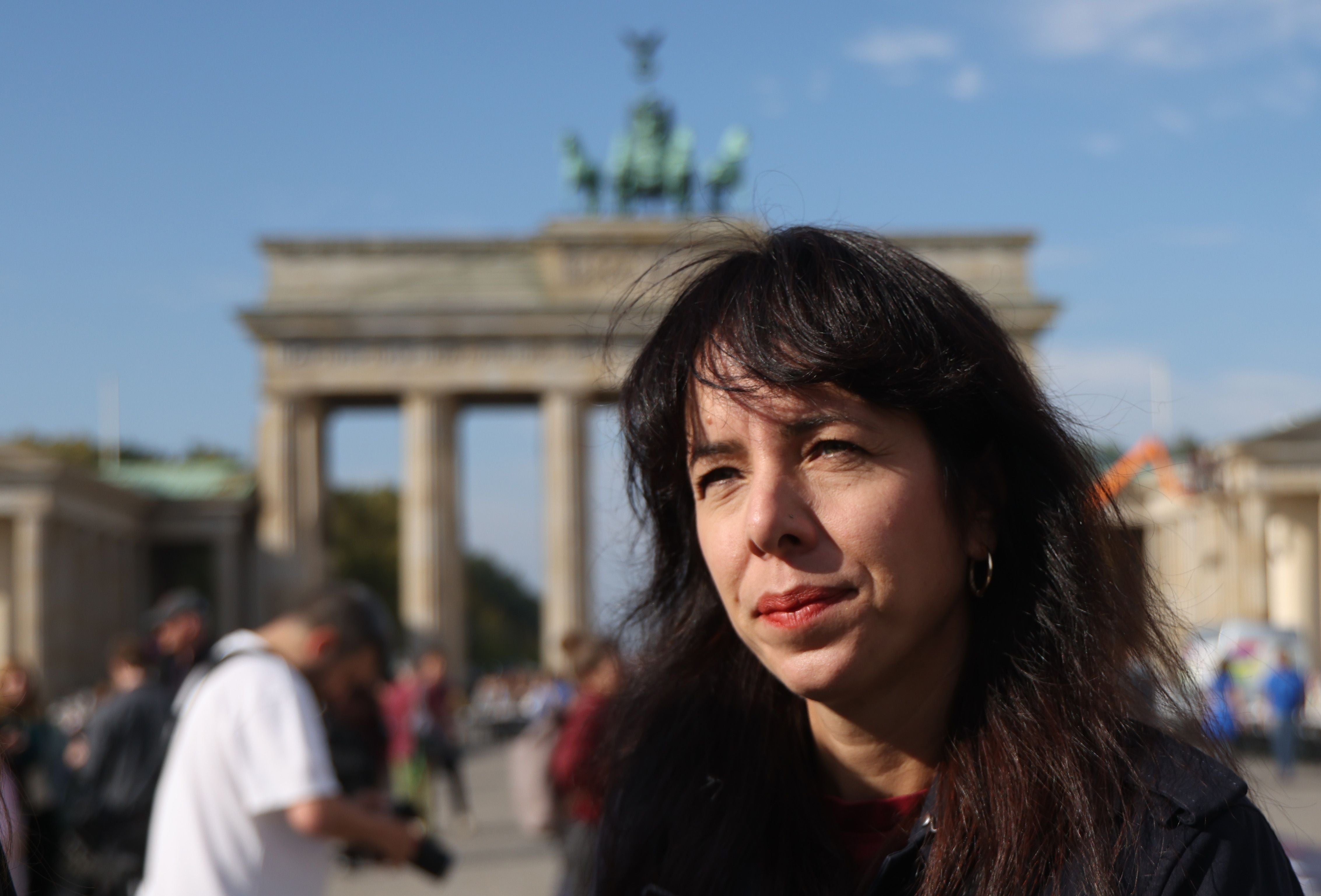 Frau vor dem Brandenburger Tor bei sonnigem Wetter, Menschen im Hintergrund.