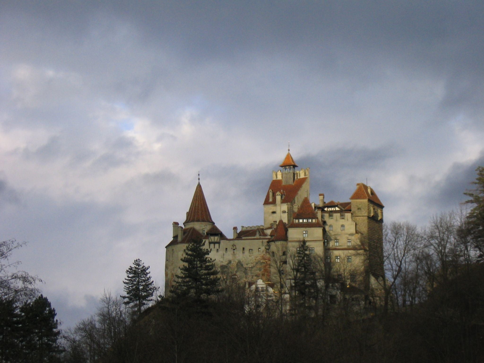 Das Schloss Bran in Rumänien mit roten Dächern, umgeben von Bäumen unter bewölktem Himmel.