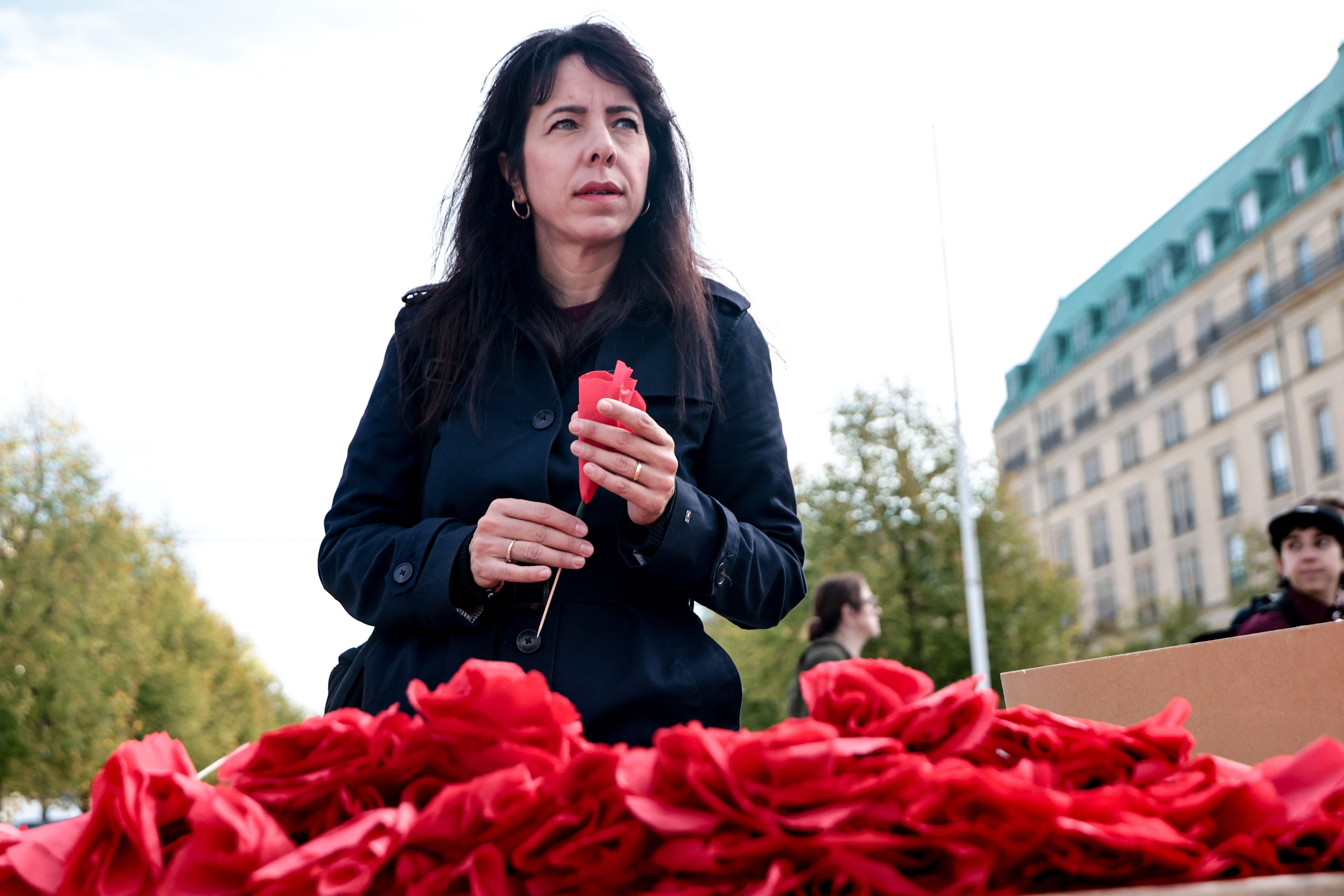 Eine Frau hält eine rote Papierblume vor einem Tisch mit vielen weiteren roten Blüten im Freien.