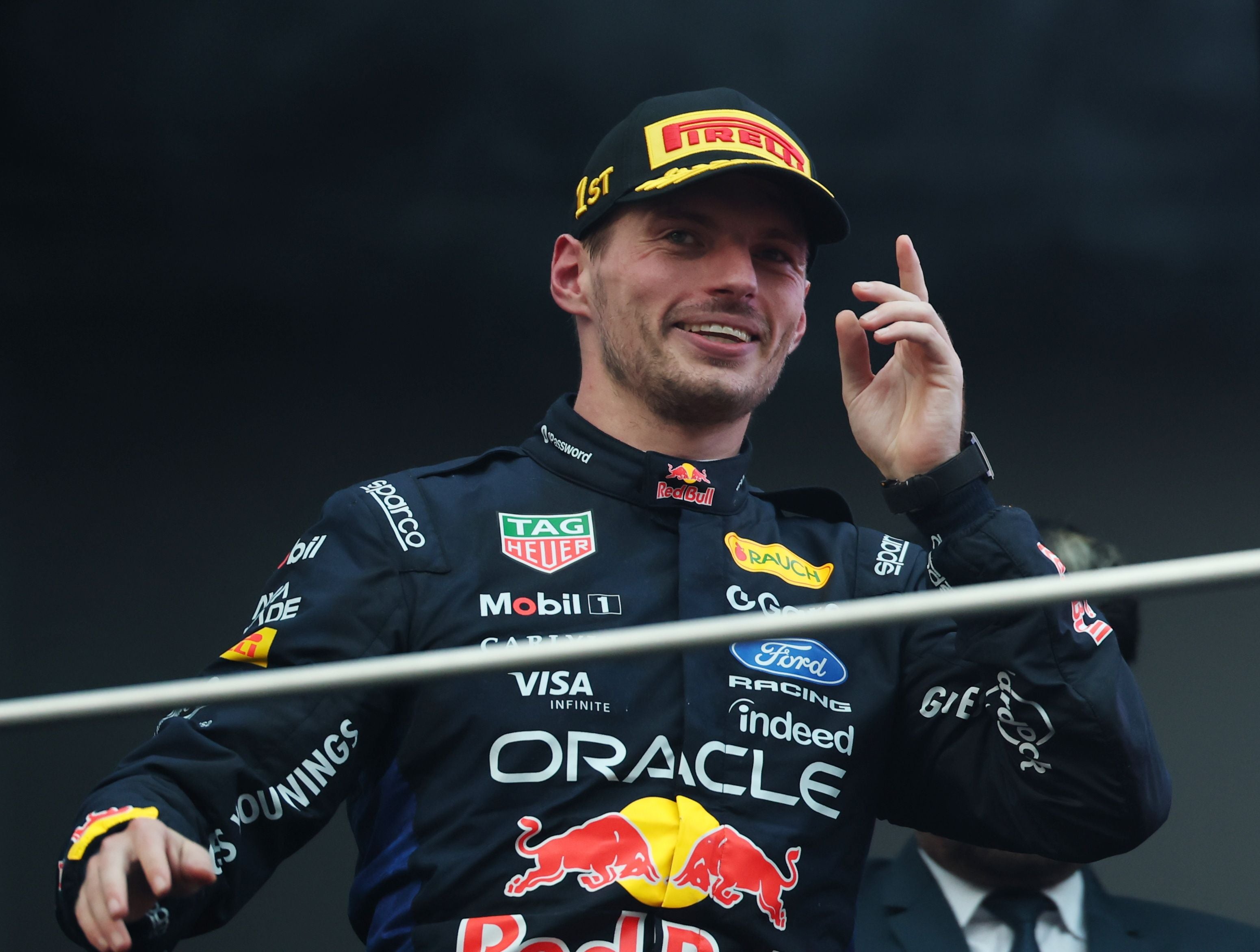 Ein Red Bull Racing Fahrer jubelt auf dem Podium mit Siegerkappe und Rennoverall.