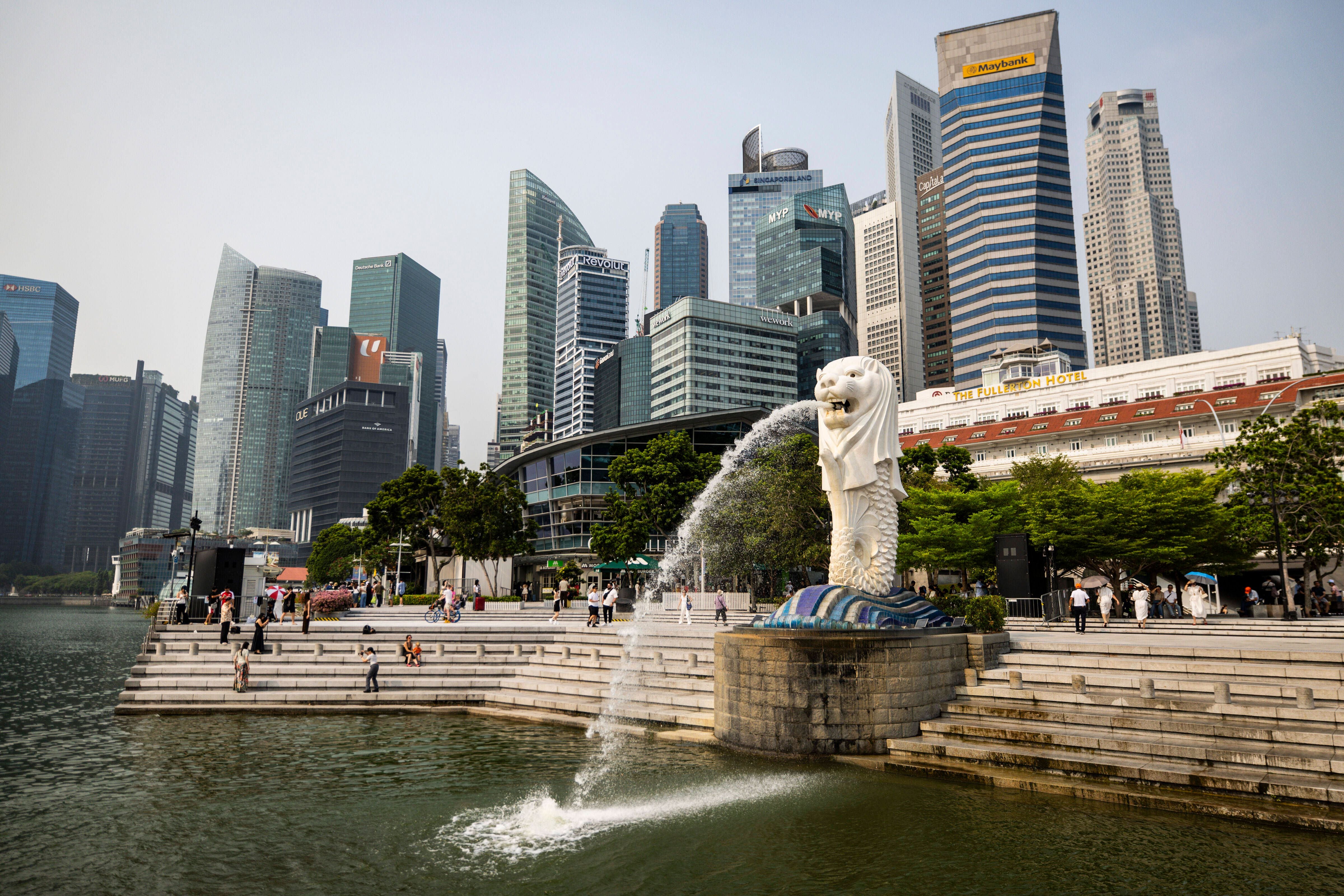 Die Merlion-Statue spuckt Wasser vor Singapurs Skyline und Marina Bay, viele Menschen sind anwesend.