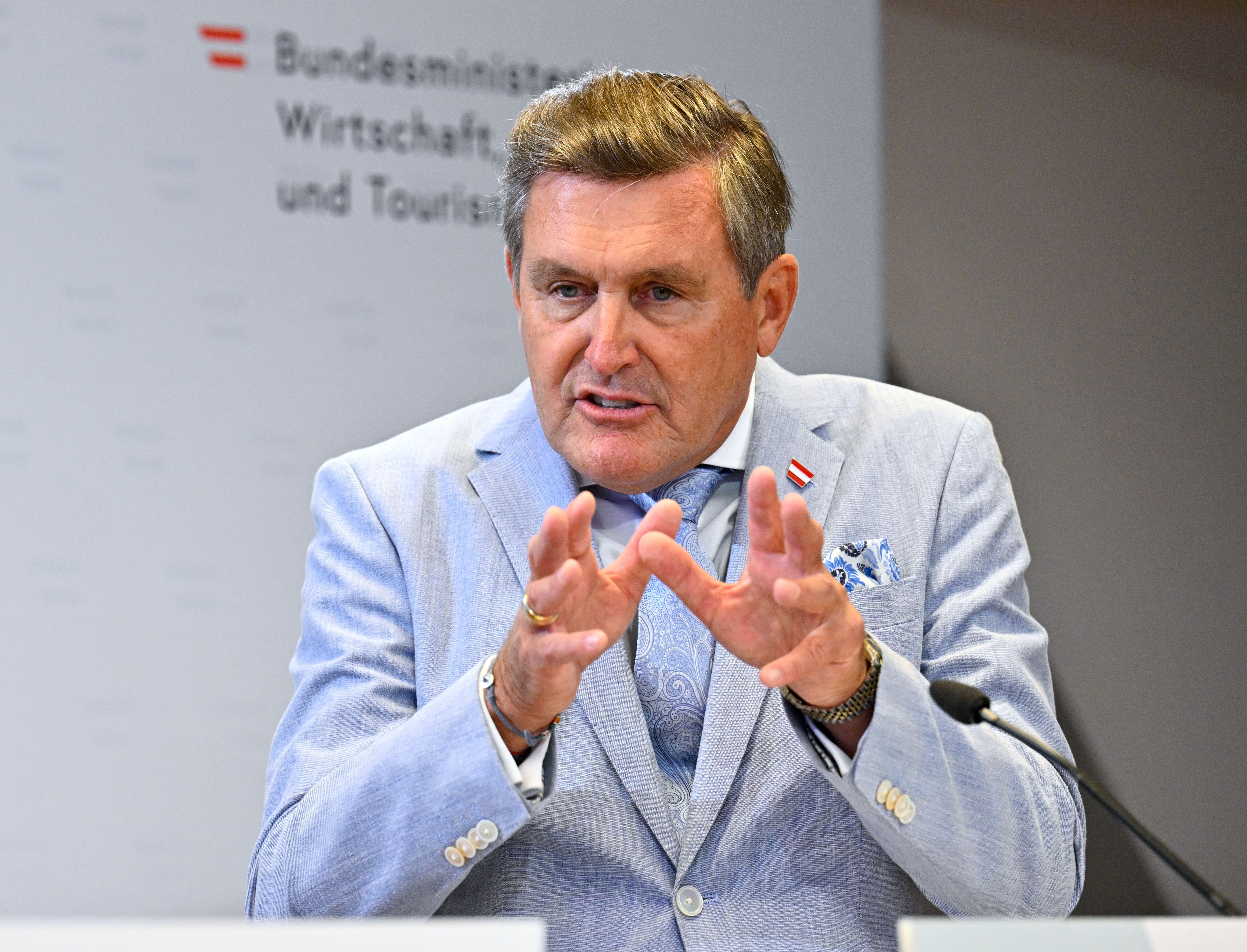 Ein Mann im hellblauen Anzug spricht bei einer Pressekonferenz vor Mikrofonen.