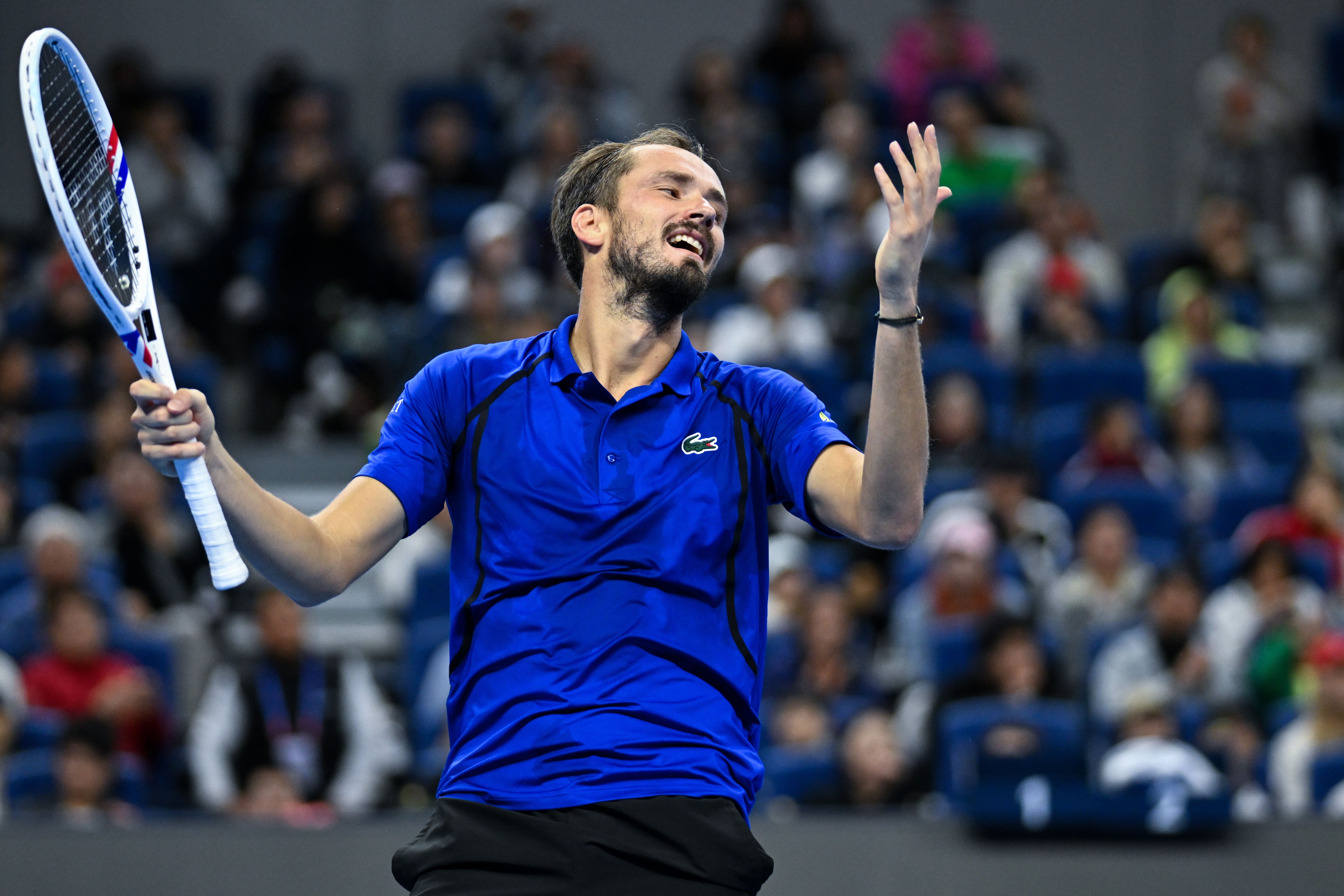 Ein Tennisspieler im blauen Shirt reagiert gestikulierend während eines Spiels in einer Halle.