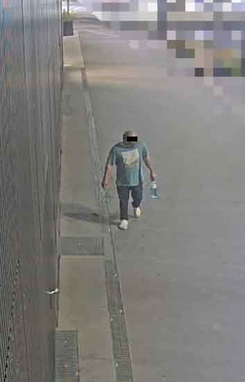 Eine Person mit verdecktem Gesicht läuft auf einem Gehweg und hält eine Flasche in der rechten Hand.