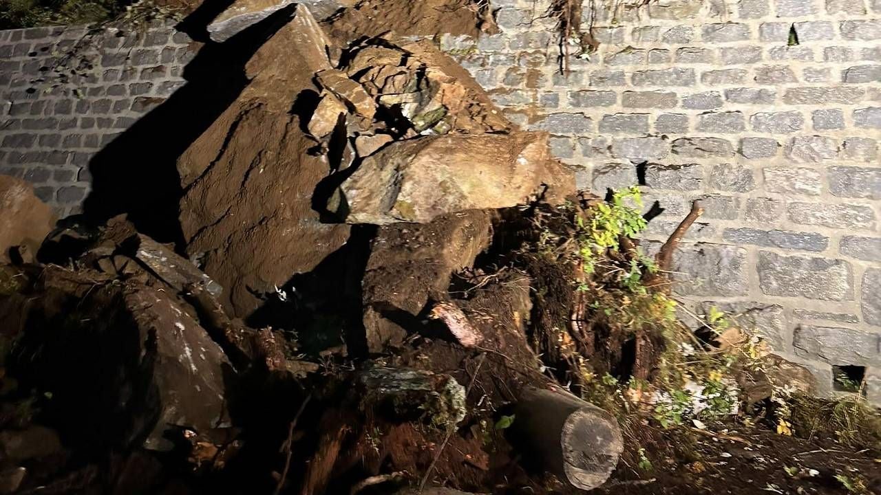 Große Felsbrocken und Erde liegen vor einer beschädigten Steinmauer im Schein einer Lampe.
