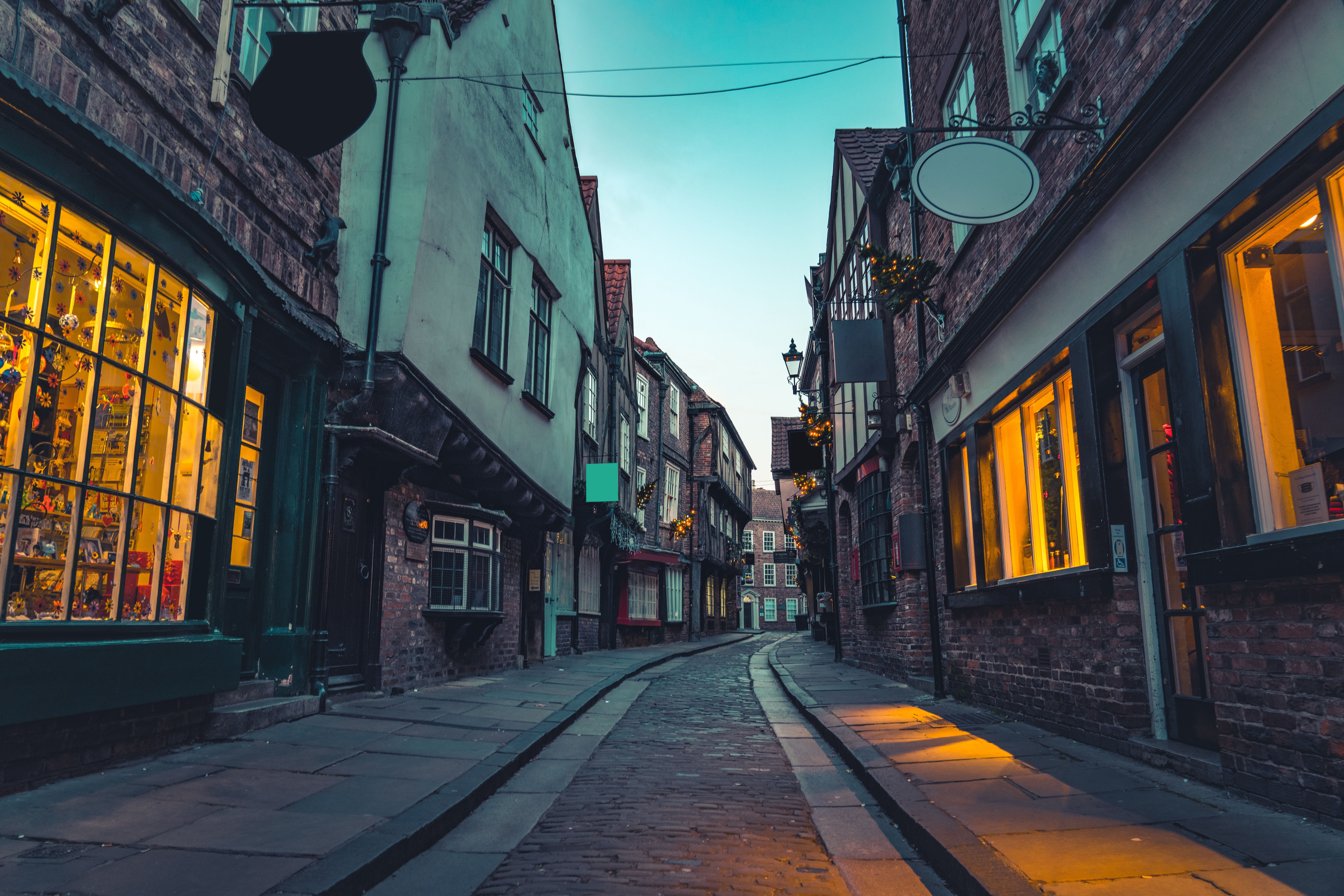 Schmale, gepflasterte Straße mit alten Fachwerkhäusern und beleuchteten Schaufenstern in York.