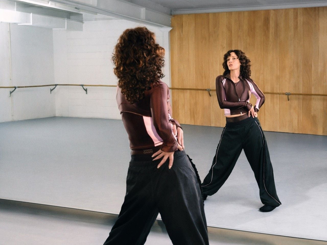 Frau tanzt vor einem Spiegel in einem leeren Tanzstudio, trägt Sportkleidung von Ganni x lululemon.