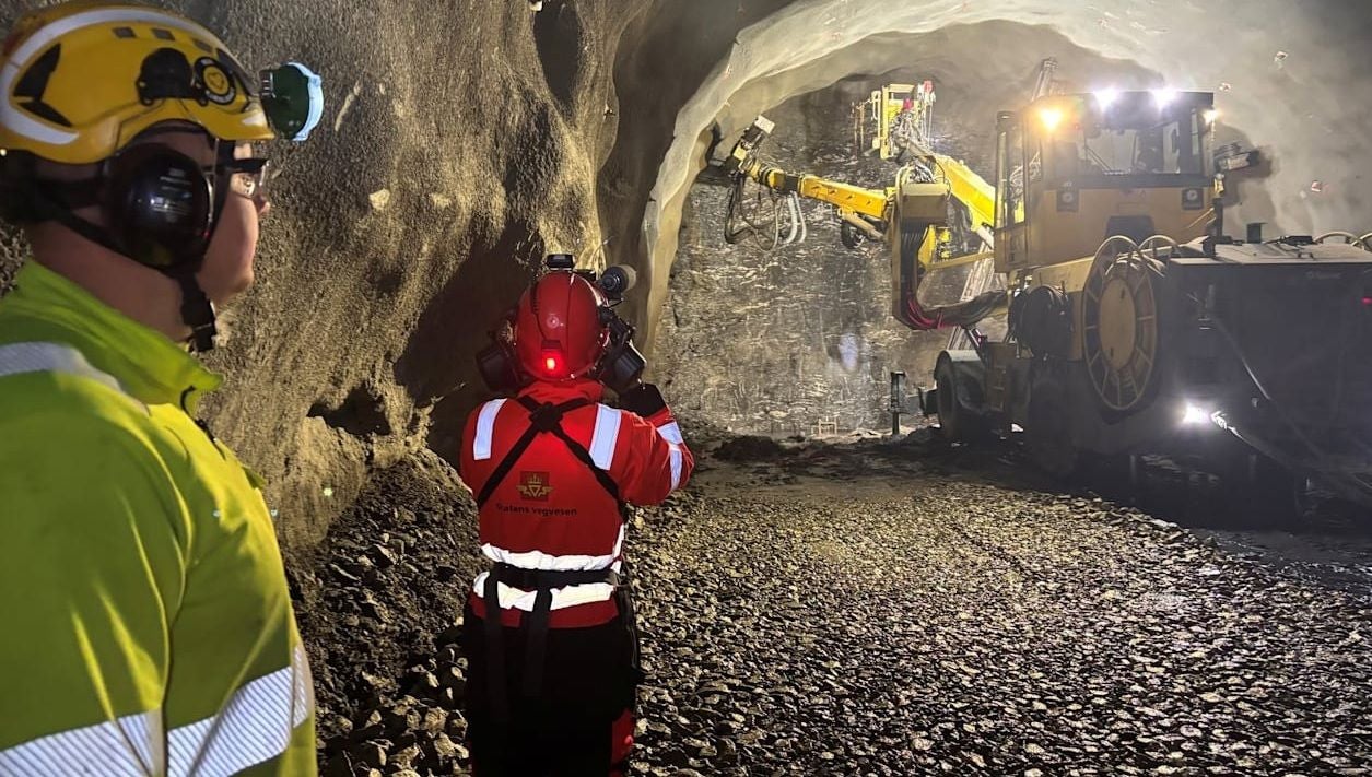 Zwei Arbeiter beobachten eine Tunnelbohrmaschine bei der Arbeit im beleuchteten Tunnel.