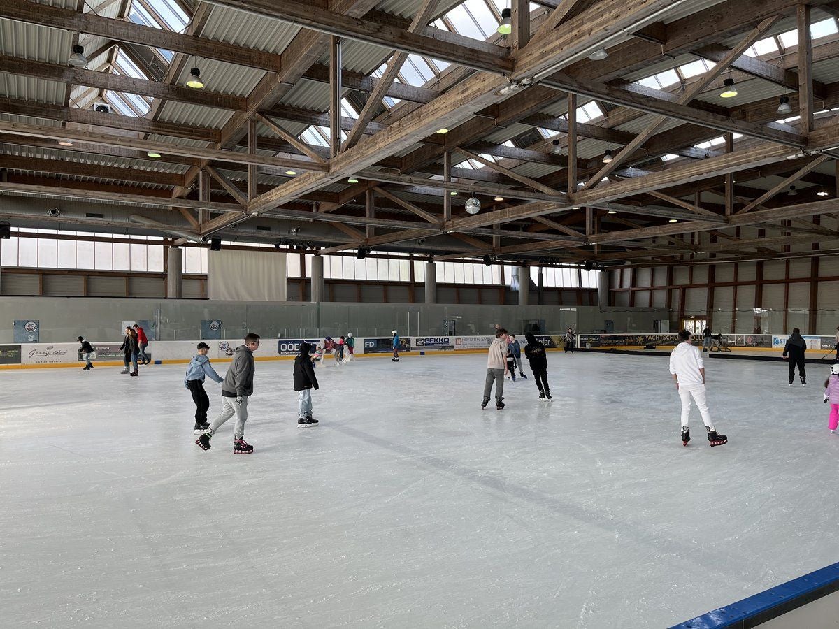Mehrere Menschen laufen auf einer überdachten Eisbahn in einer Eishalle.