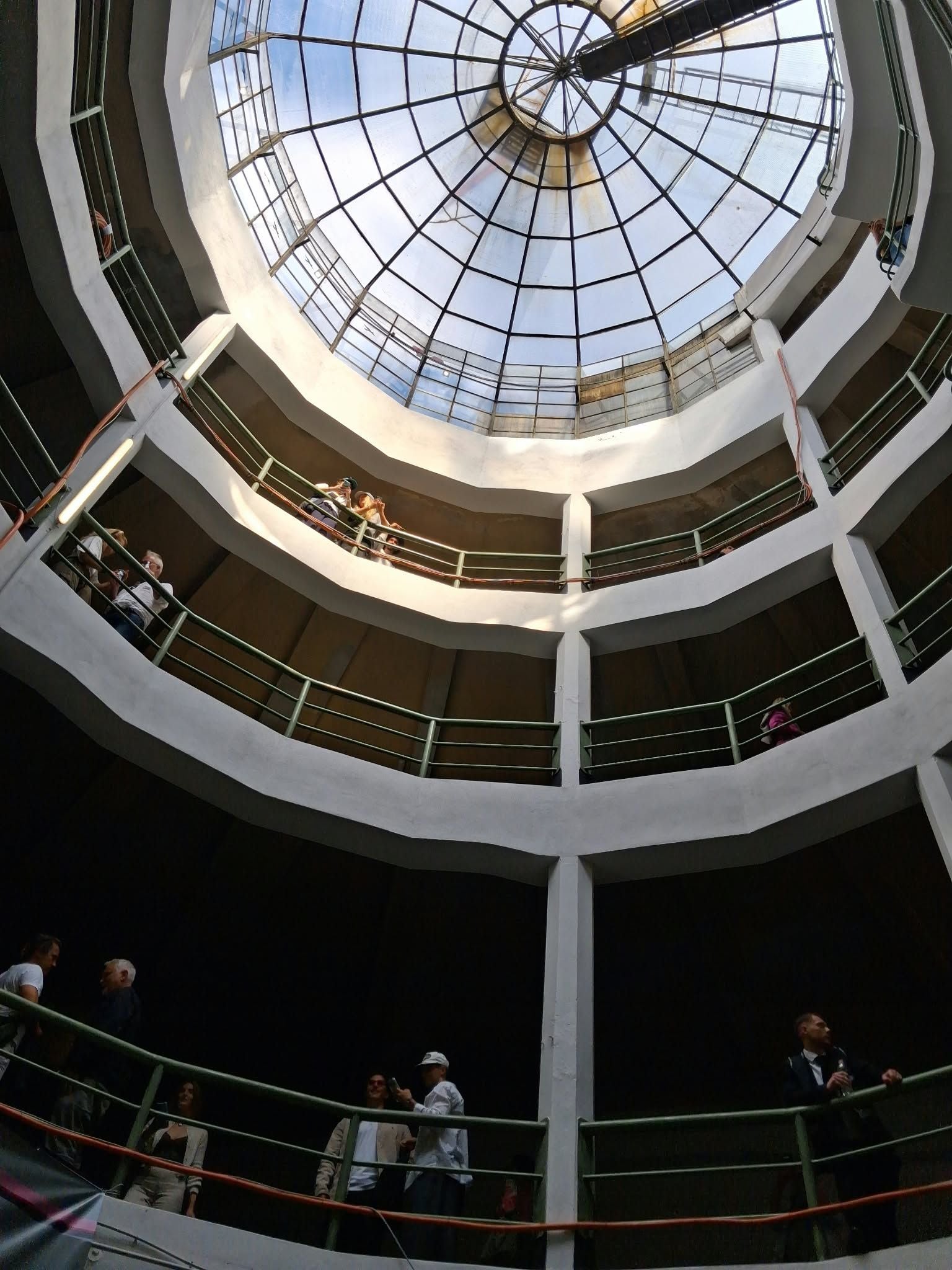 Blick nach oben in ein mehrstöckiges Parkhaus mit Glasdach und Menschen auf den Galerien.