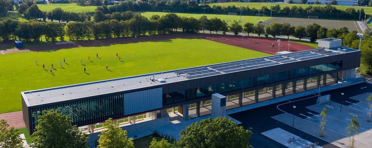 Luftaufnahme eines Sportzentrums mit Fußballfeld, Sportlern und modernem Gebäude.