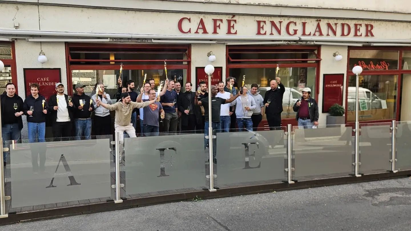 Gruppe von Menschen feiert vor dem Café Engländer und hebt ihre Gläser.