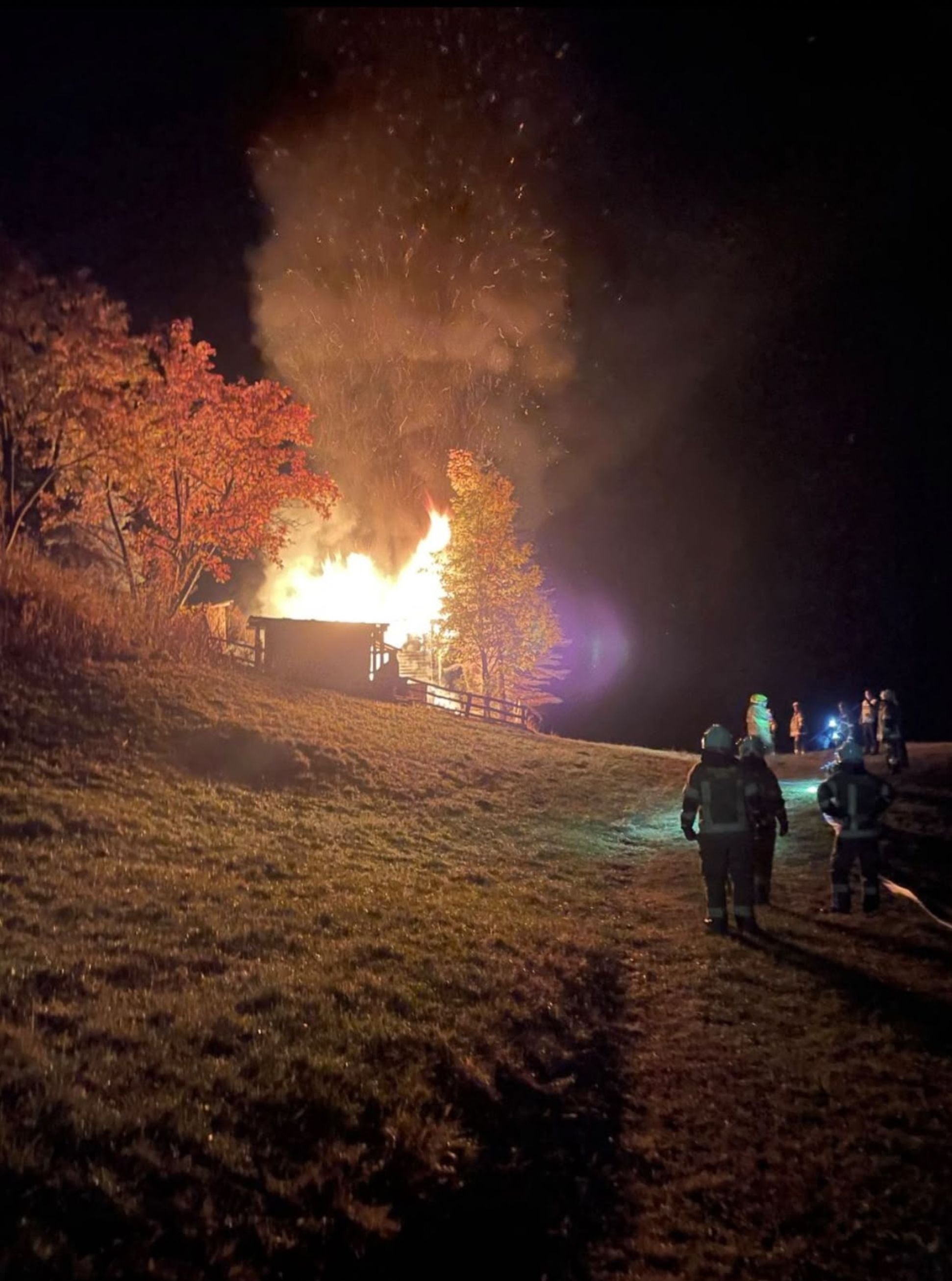 Feuerwehrleute nähern sich einem brennenden Gebäude in der Nacht, Flammen lodern stark.