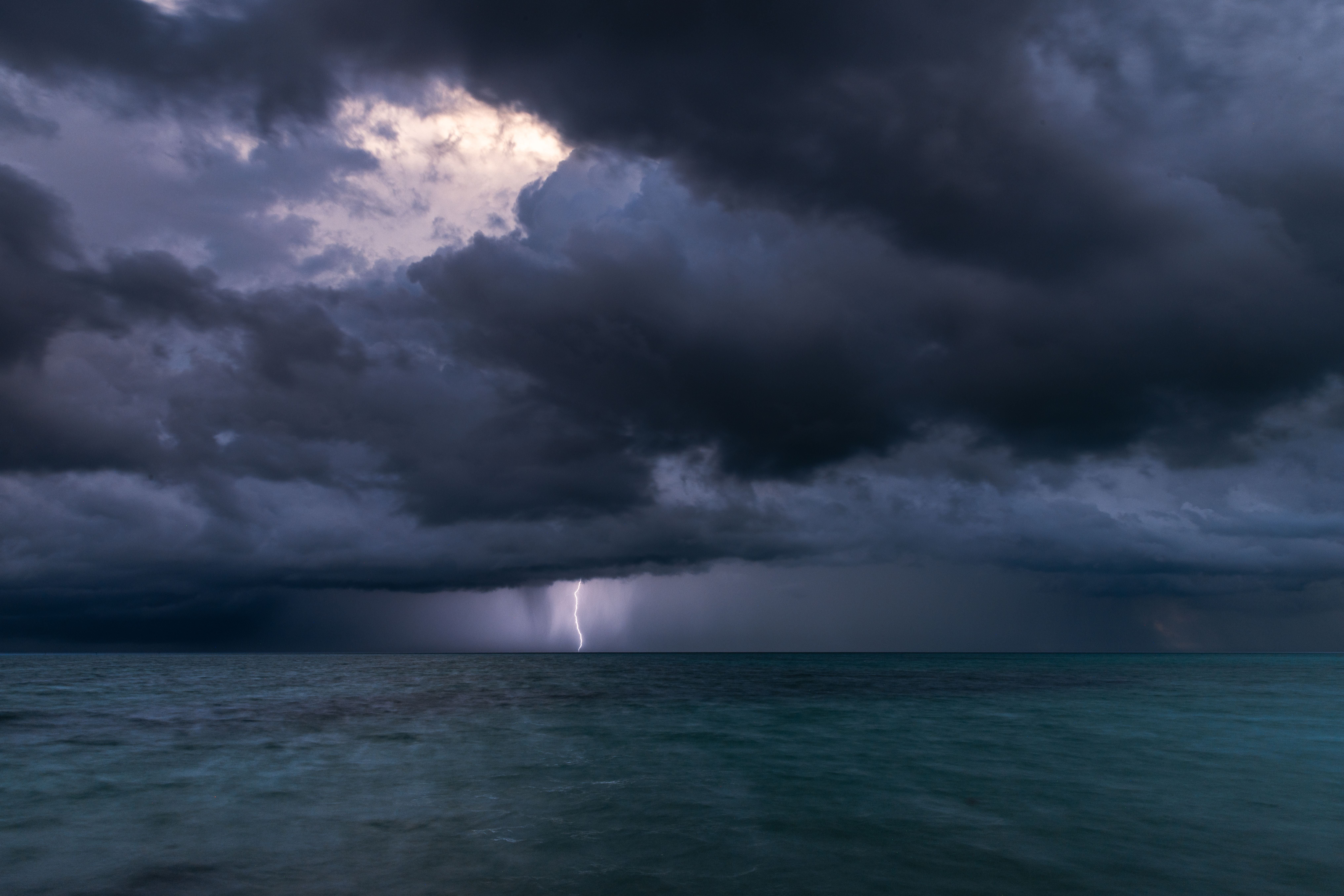 Dunkle Gewitterwolken über dem Meer, ein Blitz schlägt in der Ferne ein.