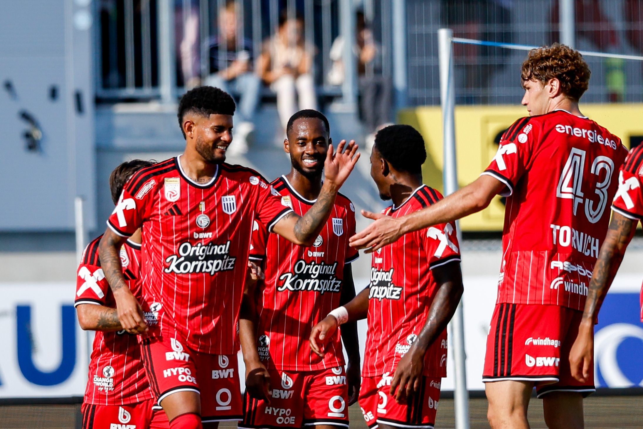 Mehrere LASK-Spieler im rot-schwarz gestreiften Trikot jubeln auf dem Feld und klatschen miteinander ab.
