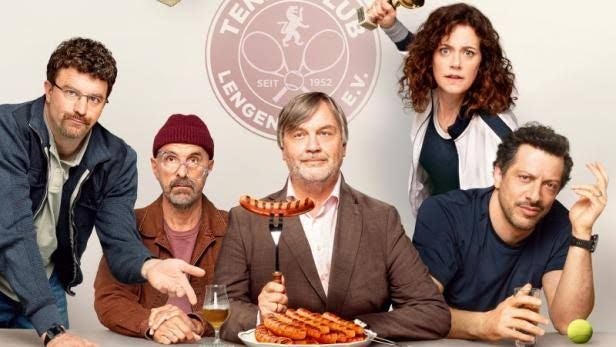 Fünf Menschen sitzen am Tisch mit Wurstteller, Getränken und Tennisclub-Logo im Hintergrund.