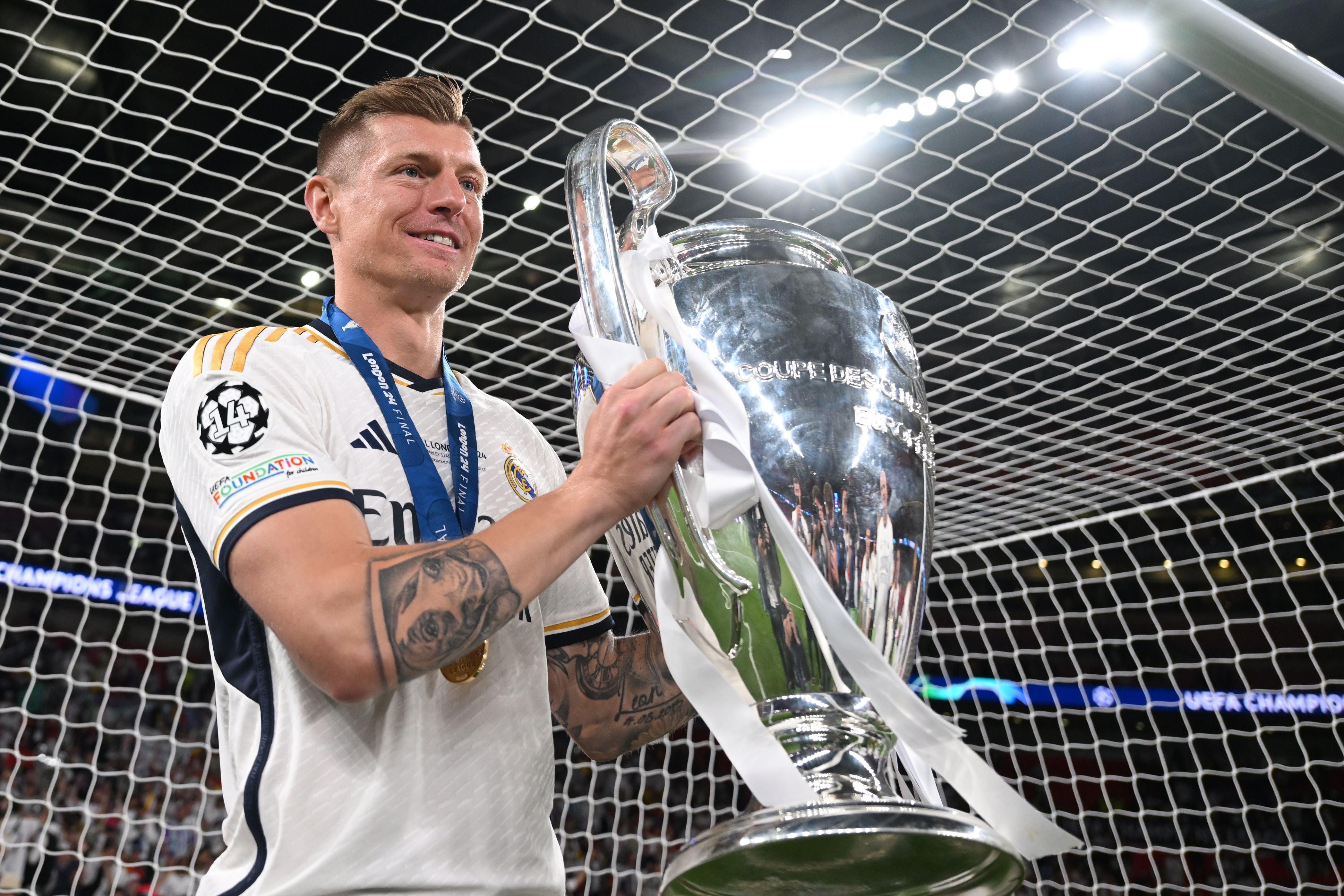 Ein Fußballspieler von Real Madrid hält den Champions-League-Pokal vor dem Tornetz.