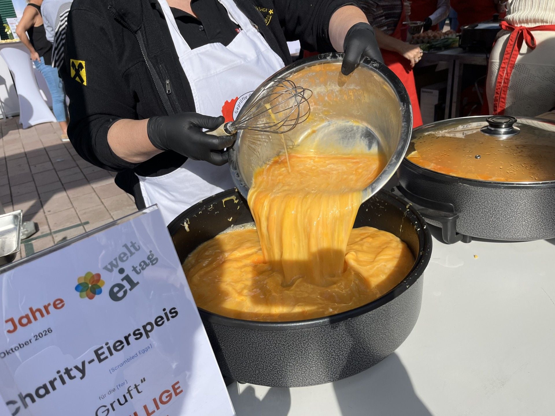 Eine Person gießt verquirlte Eier in eine große Pfanne bei einer Charity-Eierspeis am Naschmarkt.