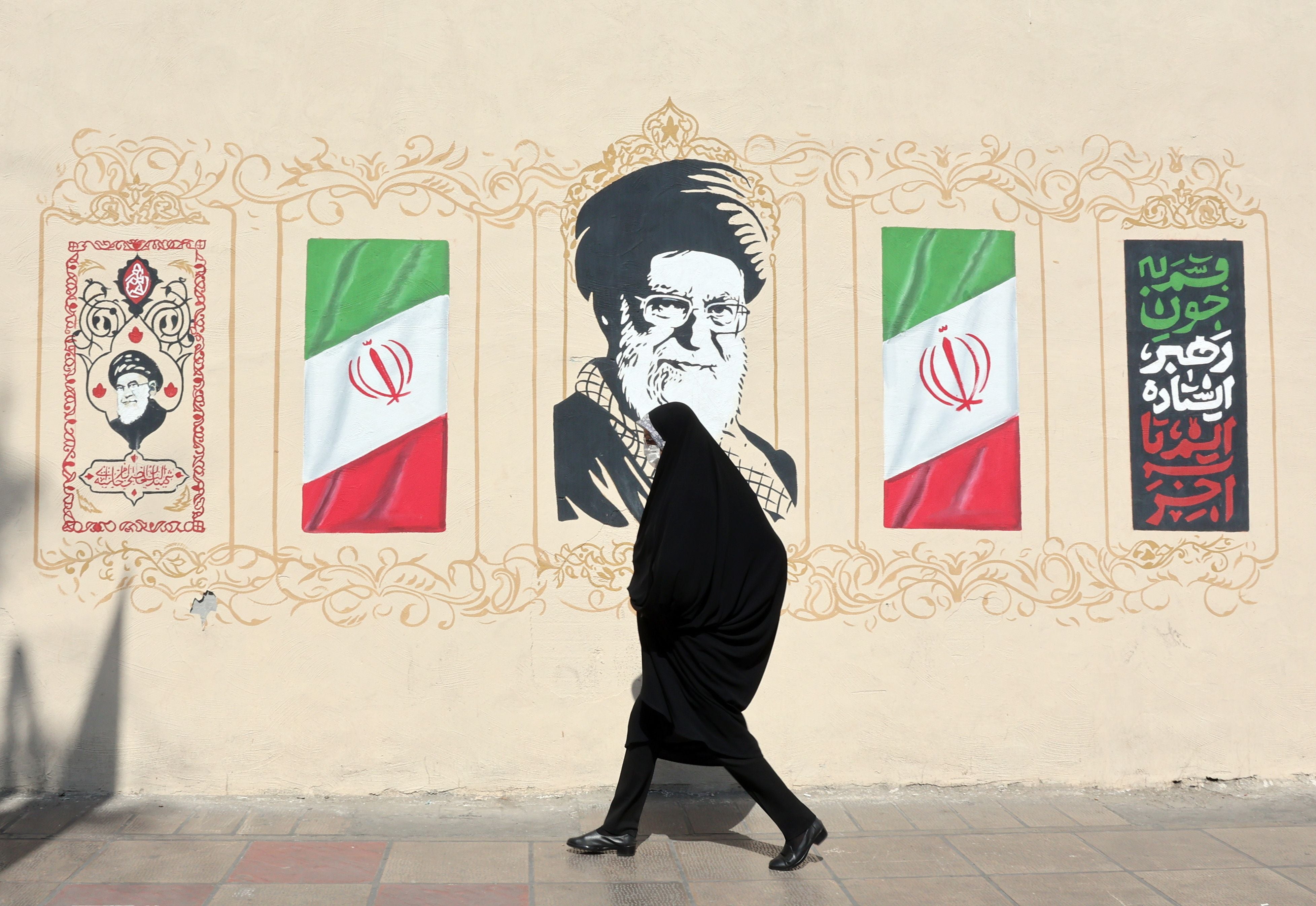 Eine verschleierte Frau geht an einem Wandbild mit Porträt und Flaggen des Iran in Teheran vorbei.