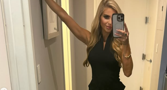 Frau macht ein Selfie im Spiegel, trägt ein schwarzes Kleid und hat langes, blondes Haar.