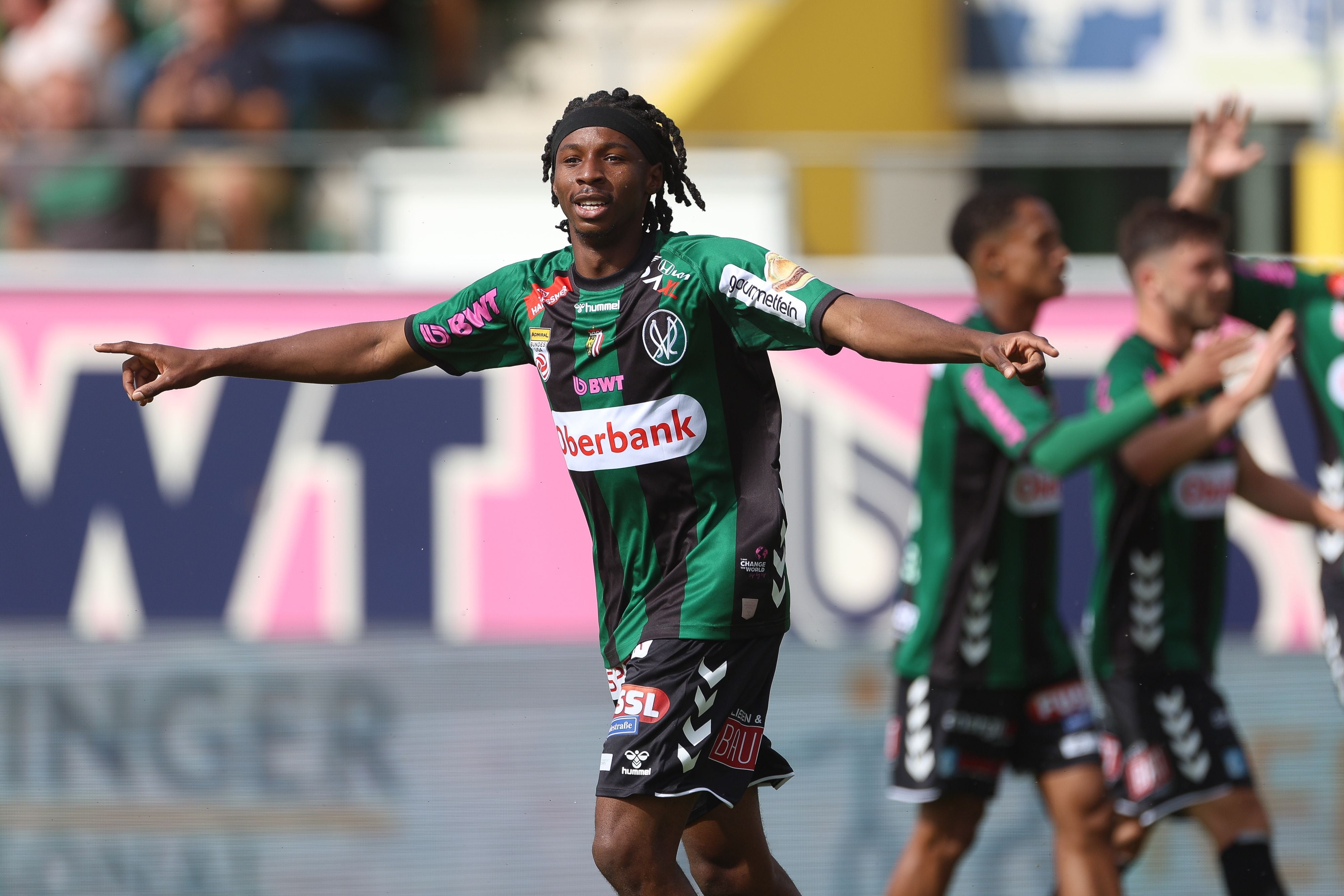 Fußballprofi Kingsley Boateng jubelt im grün-schwarz gestreiften Trikot der SV Ried mit ausgebreiteten Armen auf dem Spielfeld.