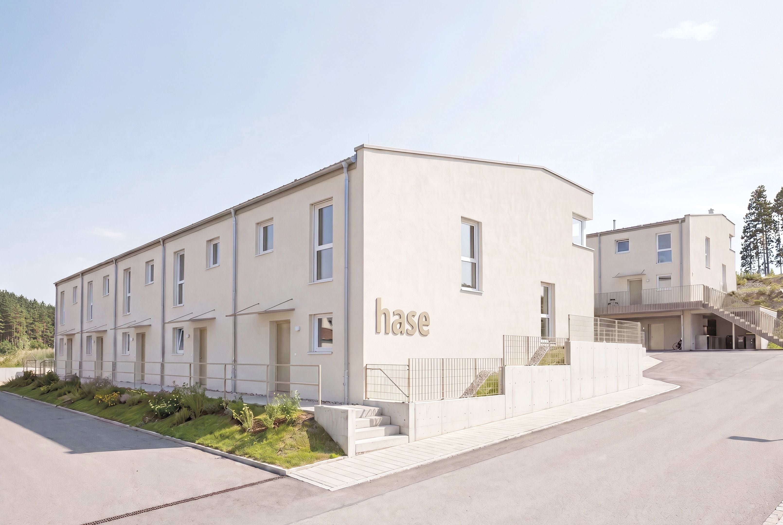 Moderne, helle Reihenhäuser mit der Aufschrift "hase" an der Fassade auf einer Wohnstraße.