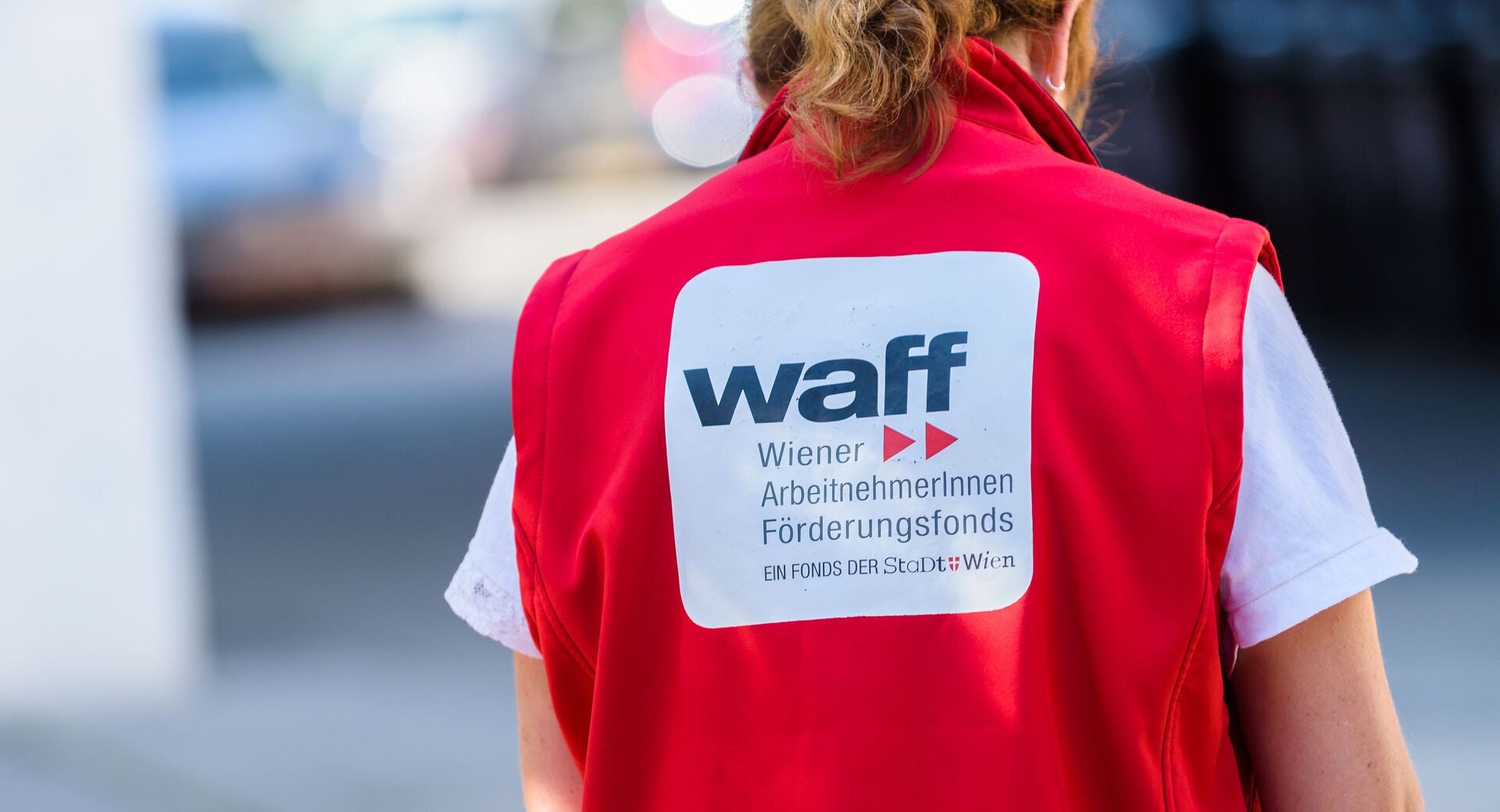 Person mit roter WAFF-Weste von hinten, Schriftzug des Wiener ArbeitnehmerInnen Förderungsfonds sichtbar.