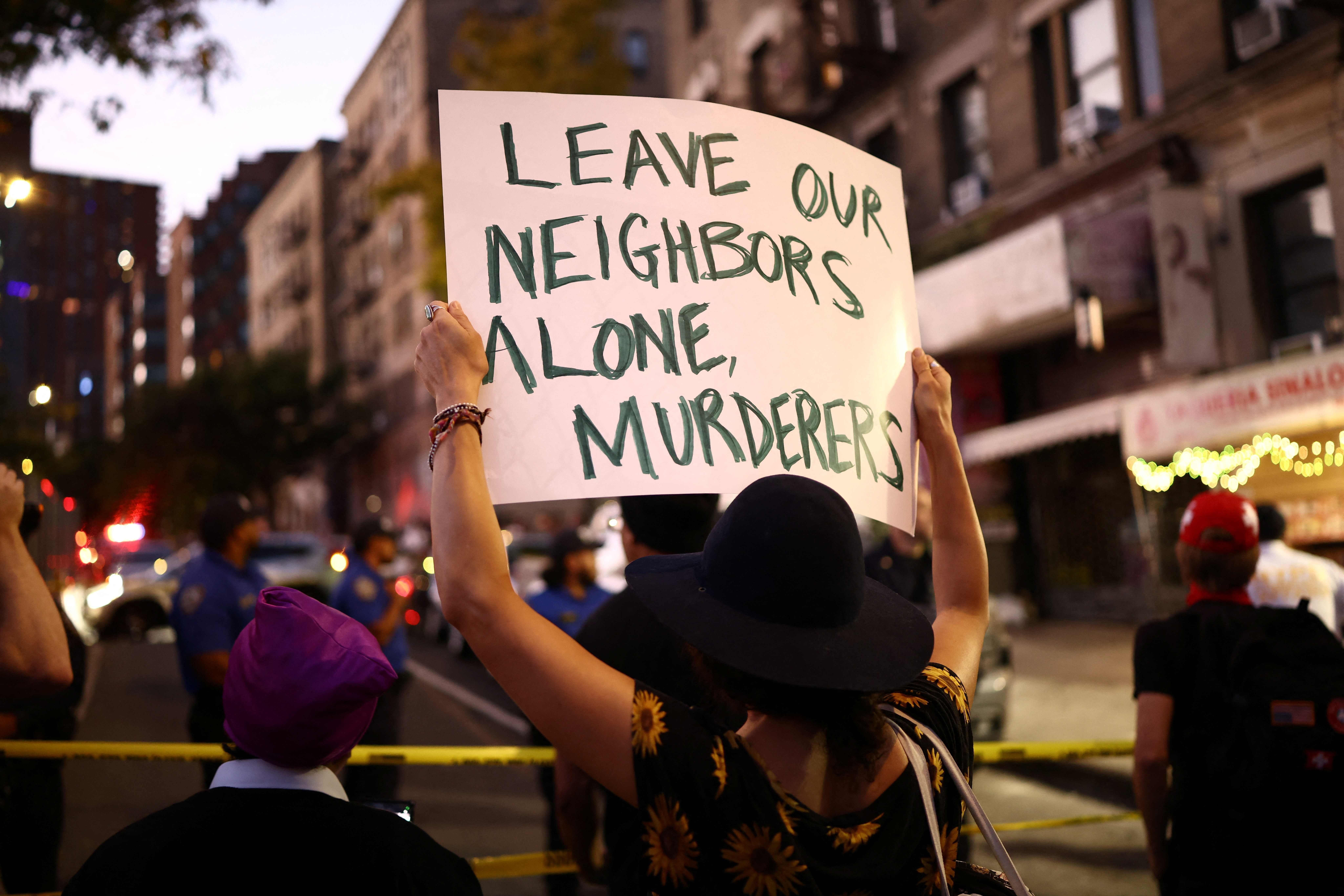 Person hält Protestplakat mit der Aufschrift „Leave our neighbors alone, murderers“ auf einer Straße.