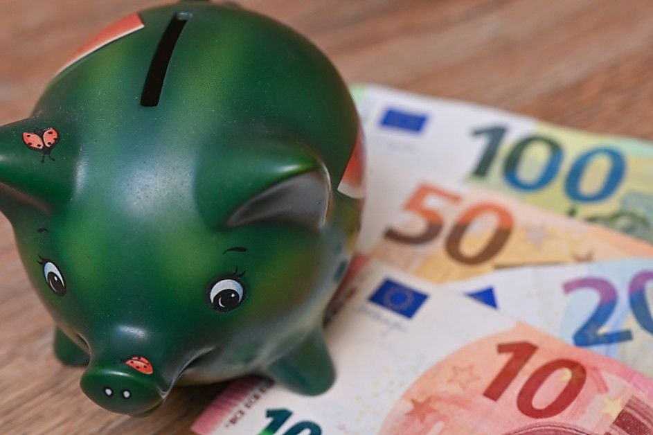 Grünes Sparschwein neben mehreren Euro-Geldscheinen auf einem Holztisch.