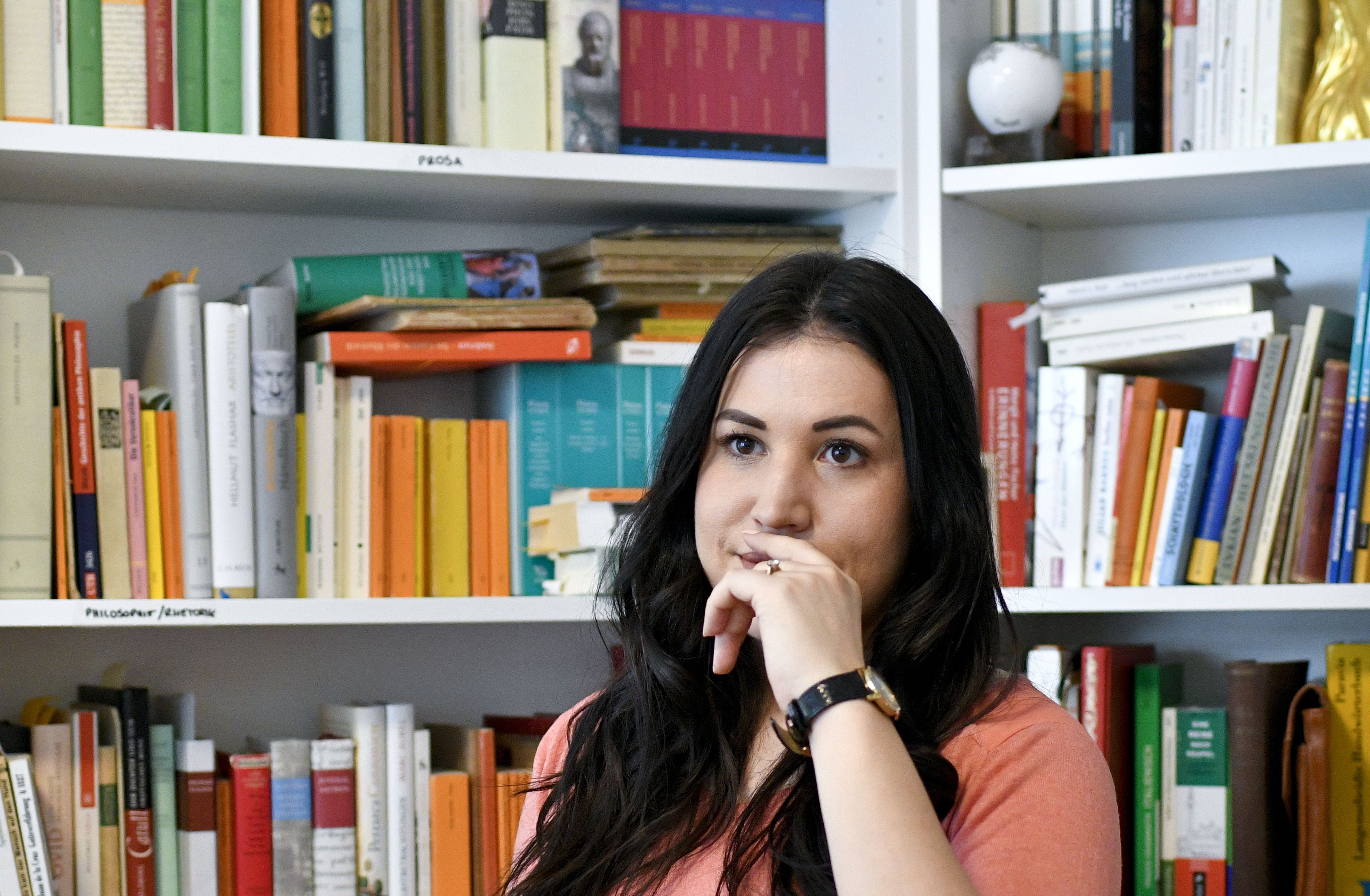 Eine Frau sitzt nachdenklich vor einem Bücherregal voller Bücher.