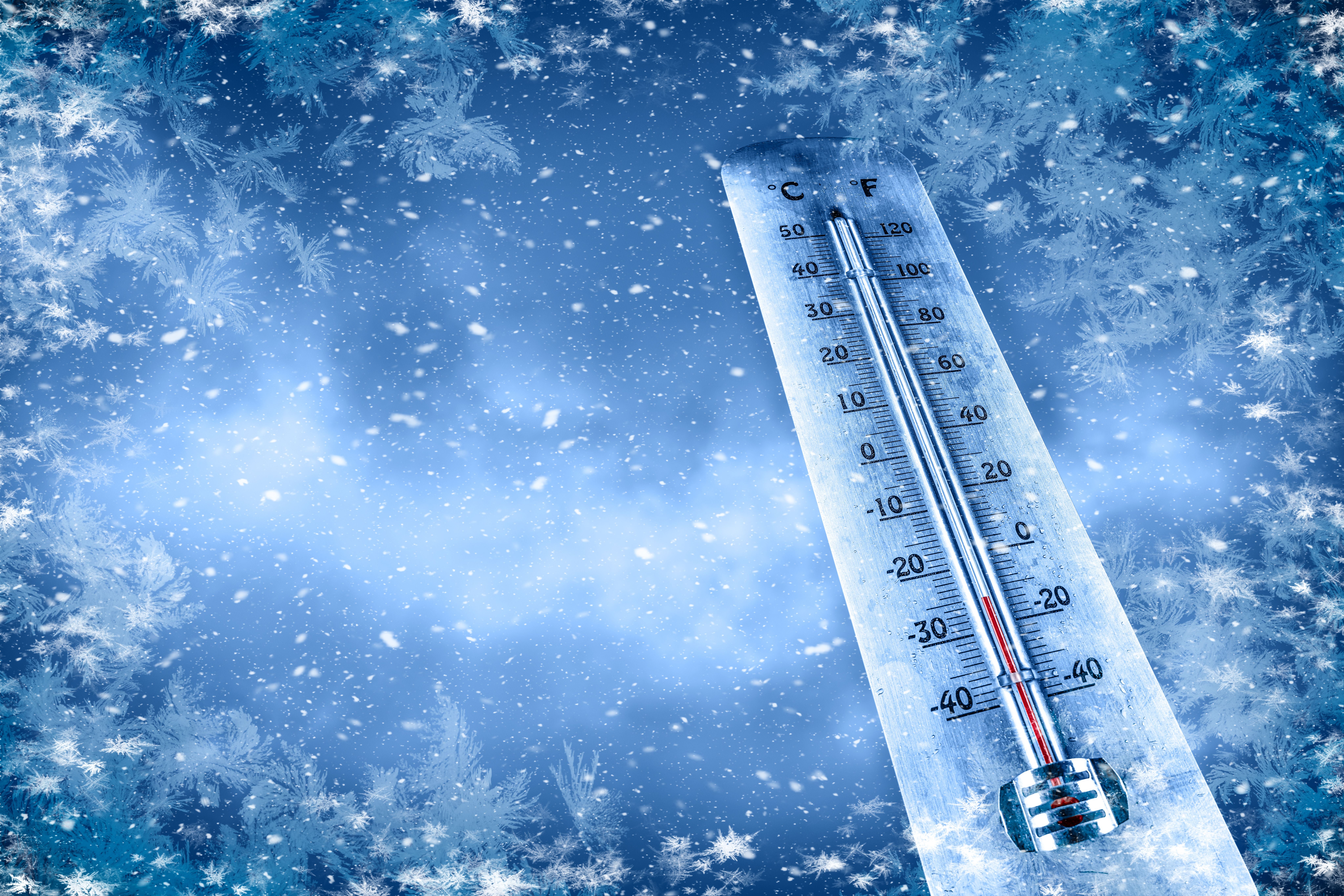 Thermometer zeigt sehr kalte Temperatur, umgeben von Schnee und frostigen Mustern.