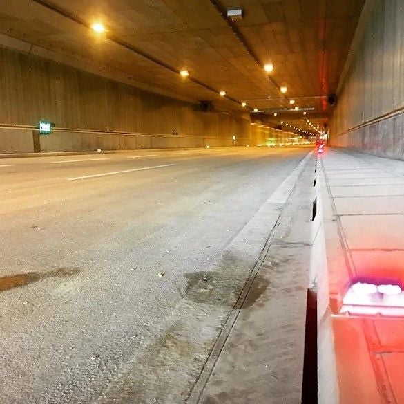 Leerer, beleuchteter Straßentunnel mit leuchtenden roten Lichtern am rechten Rand.