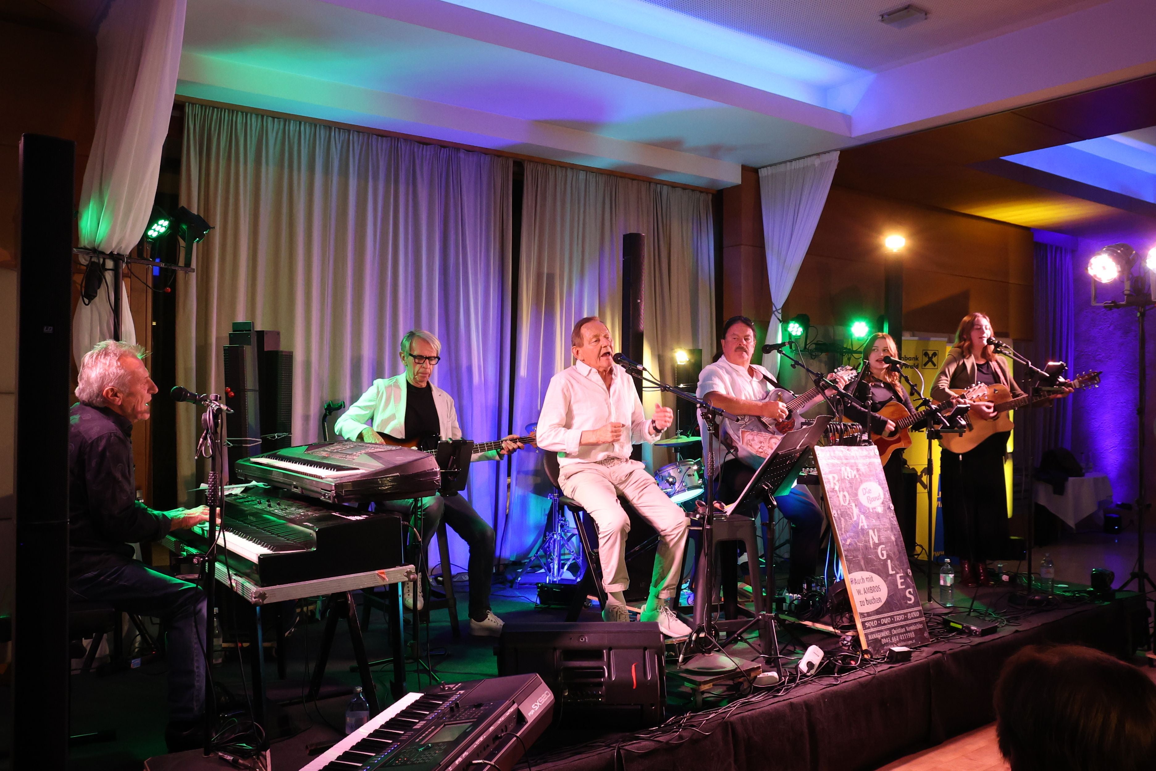 Mehrere Musiker spielen auf einer Bühne bei einem Live-Konzert in einem Innenraum.