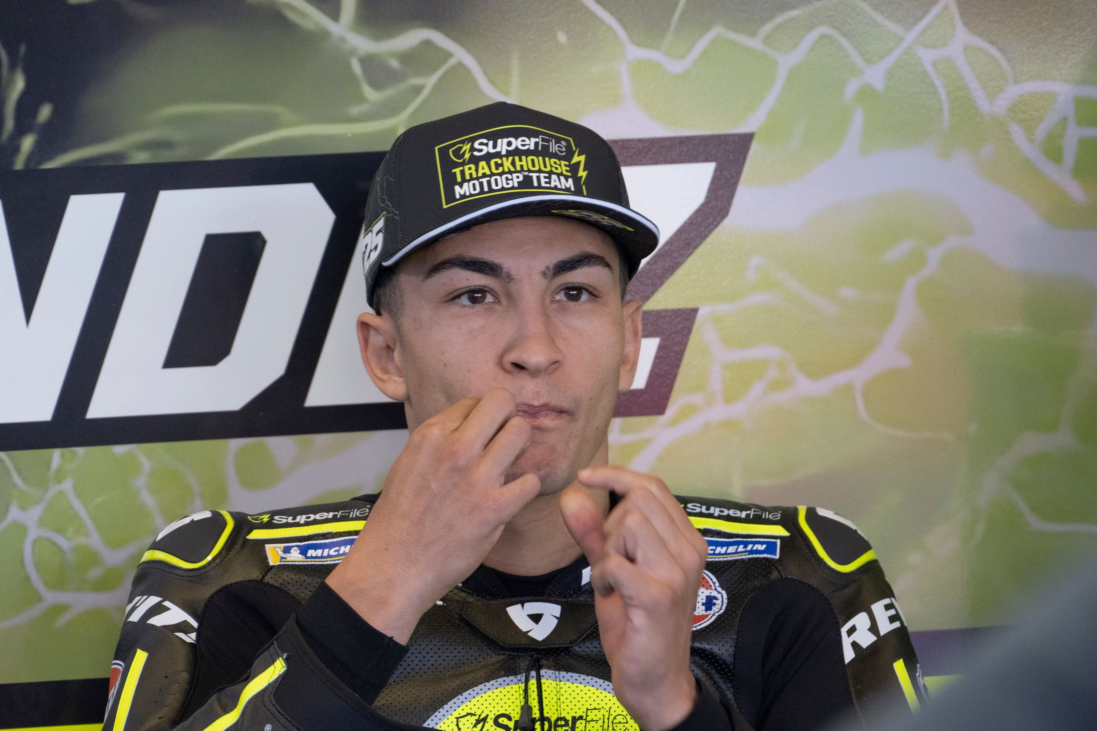 Raul Fernandez vom Trackhouse-Aprilia-Team sitzt mit schwarzer Kappe und Lederkombi bei einer Pressekonferenz am Mikrofon.