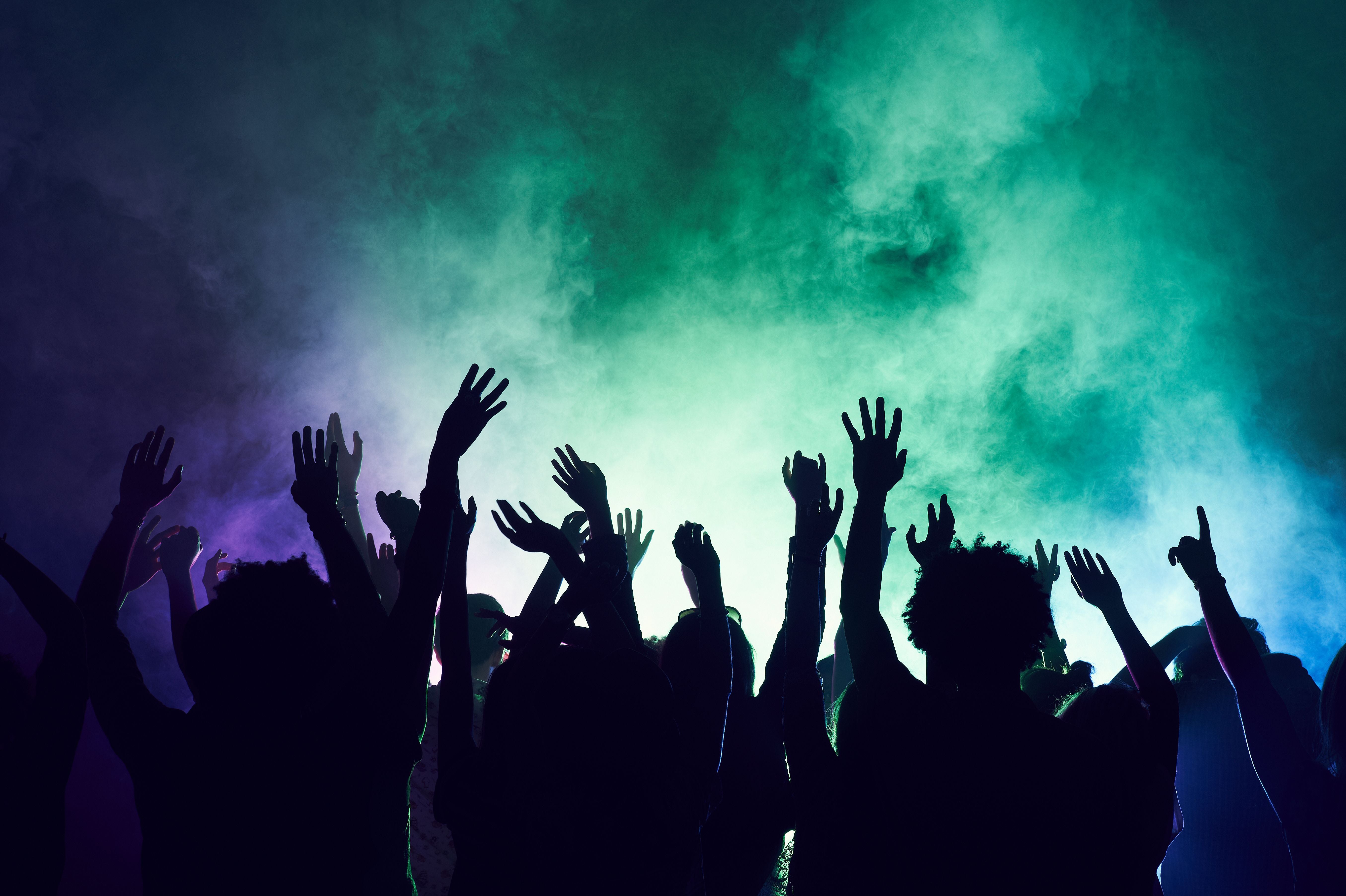 Menschenmenge auf einer Party oder einem Konzert hebt die Hände in die Luft, bunte Lichter und Nebel.