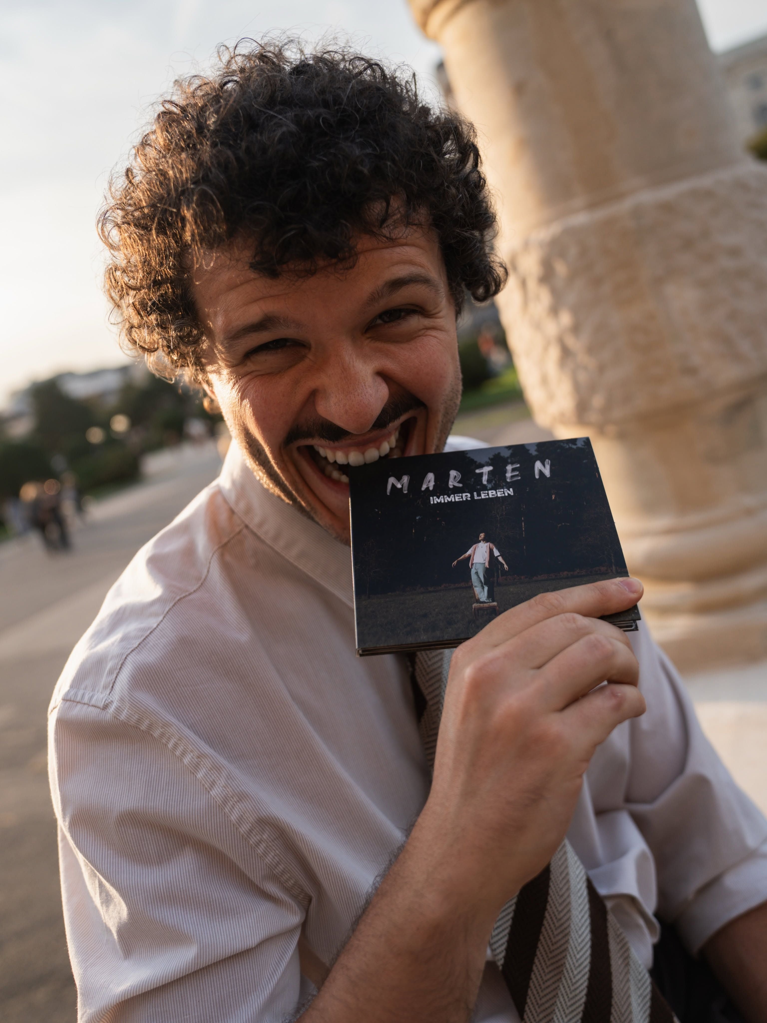 Ein lachender Mann hält eine CD mit der Aufschrift „Marten – Immer Leben“ in der Hand.