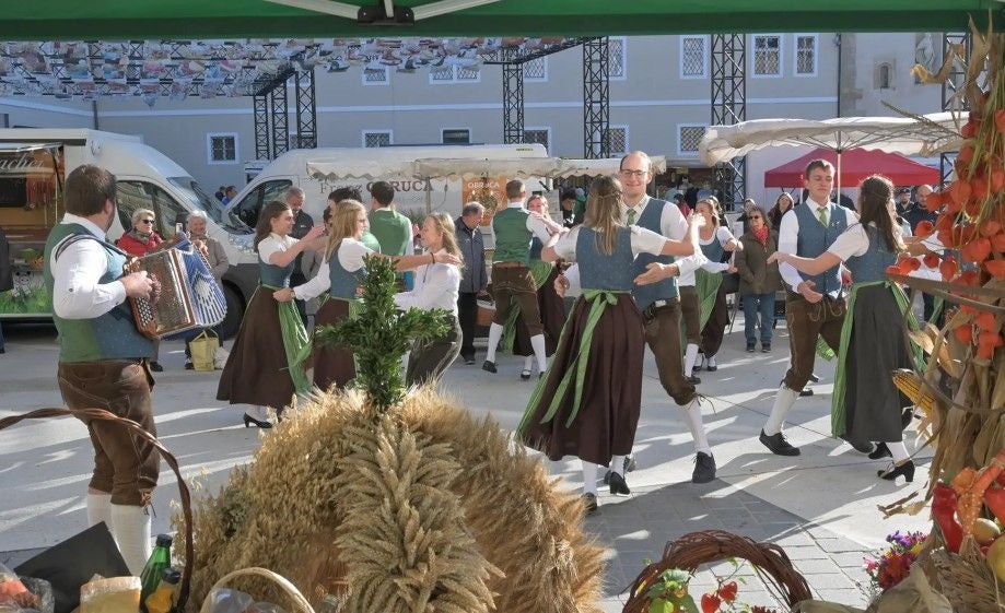 Tanzpaare in Tracht tanzen beim Erntedankfest in St. Pölten, ein Musiker spielt Ziehharmonika.