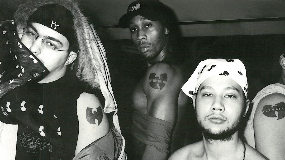 Drei Männer mit Wu-Tang Clan Tattoos und passender Kleidung posieren vor der Kamera.