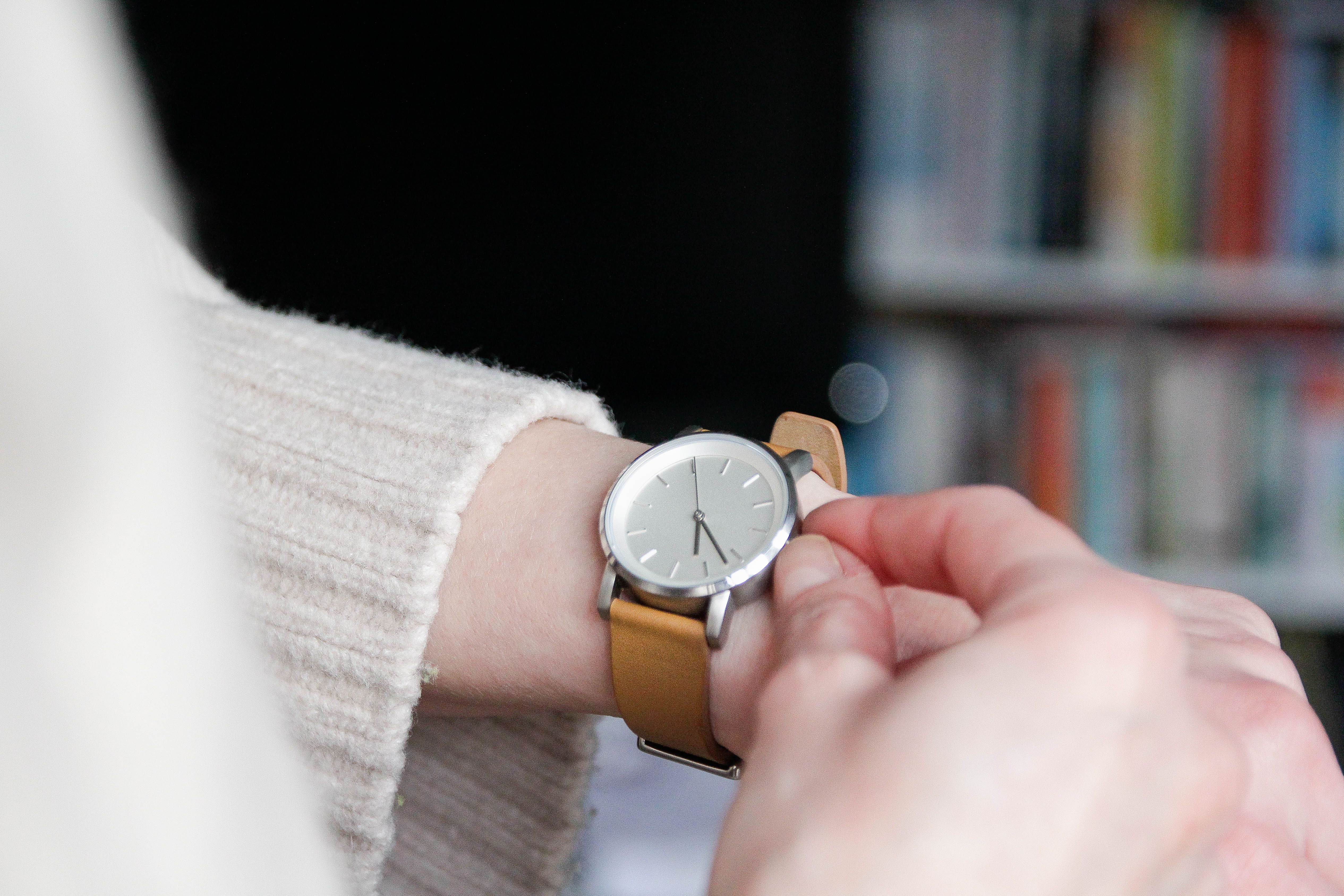 Eine Person stellt eine Armbanduhr mit braunem Lederarmband ein.