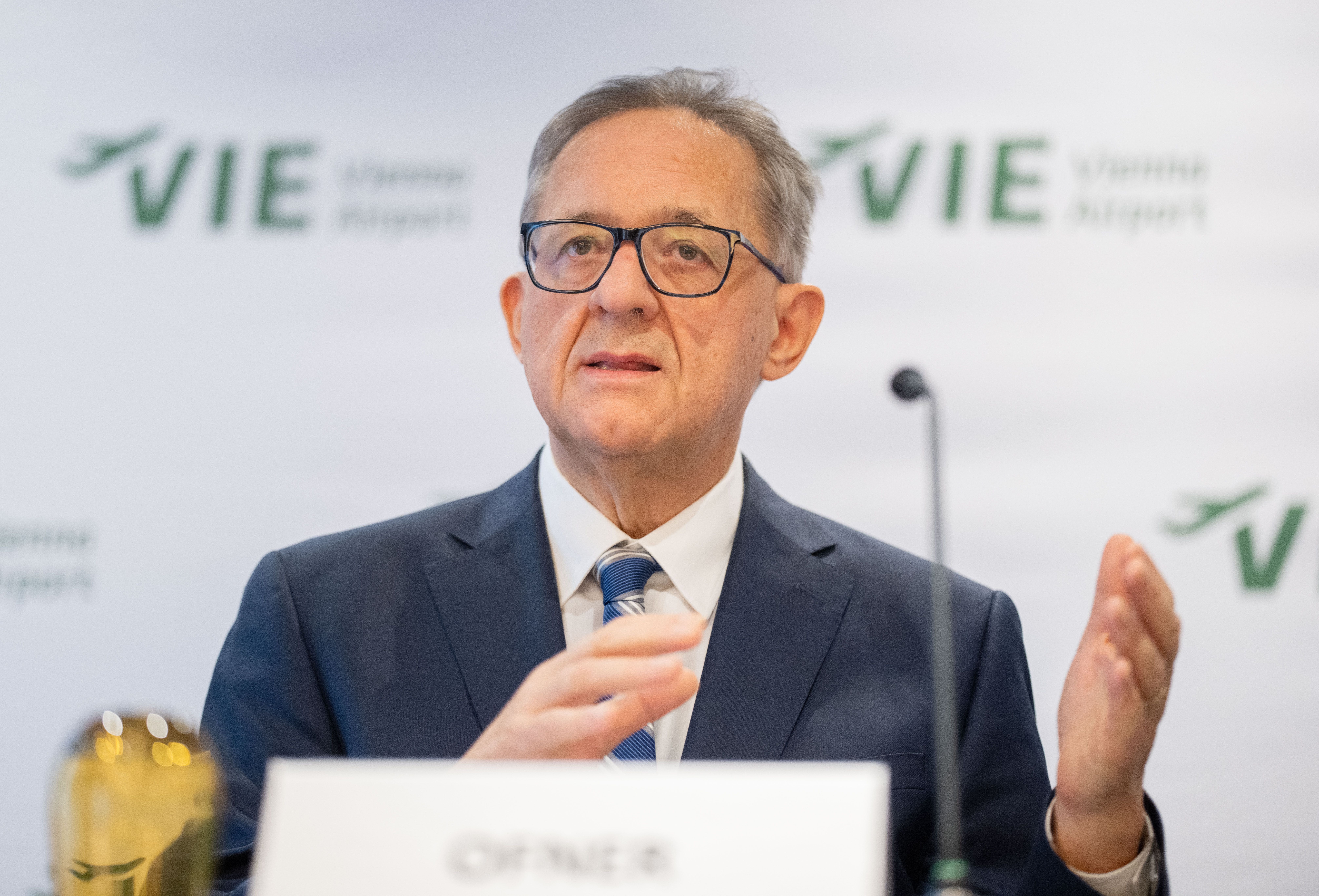Ein Mann im Anzug spricht auf einer Pressekonferenz am Flughafen Wien.