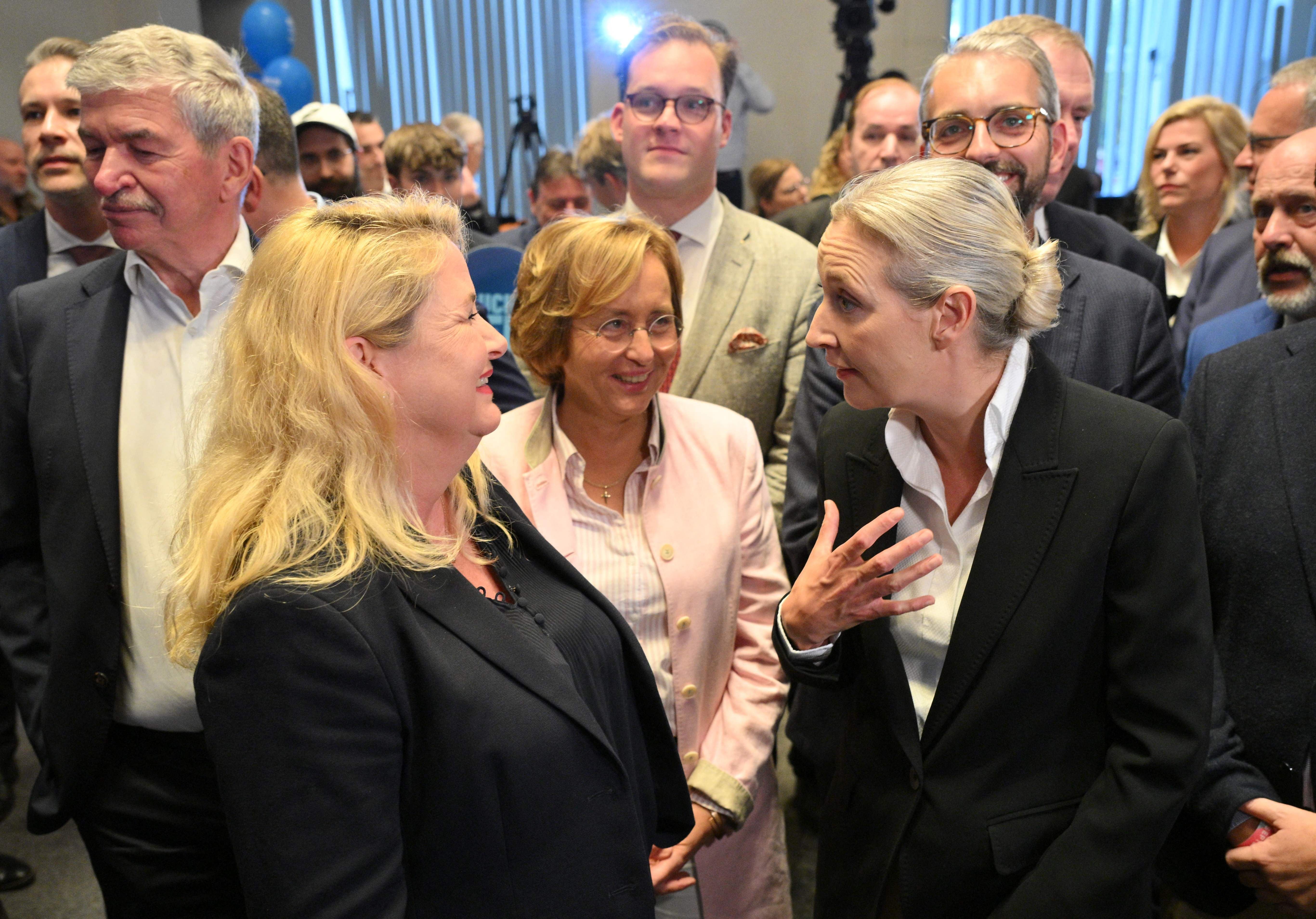 Mehrere Menschen in Geschäftsanzügen unterhalten sich bei einer Wahlveranstaltung in Berlin.