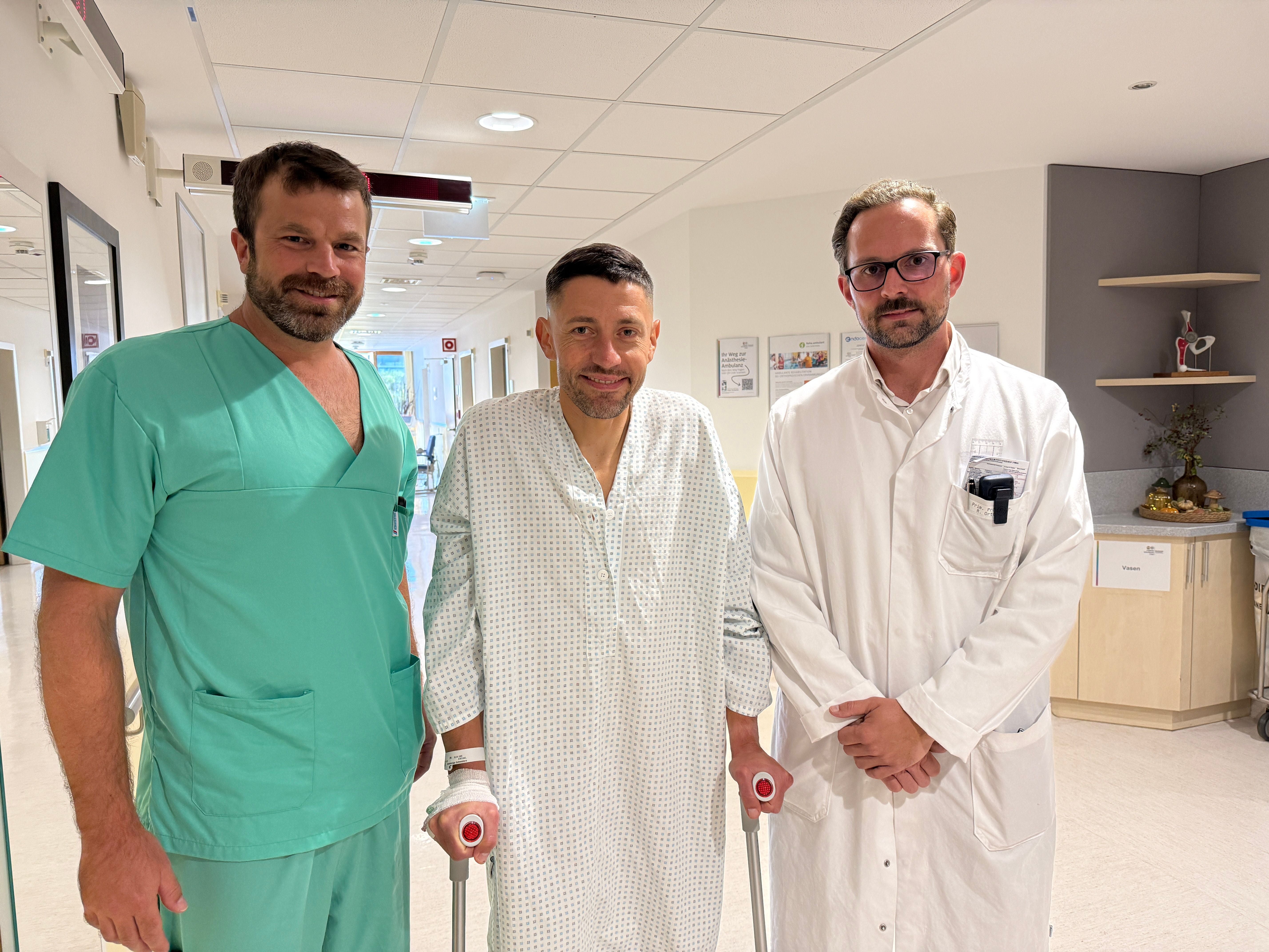 Drei Männer stehen im Krankenhausflur, einer mit Krücken nach einer Hüftoperation.