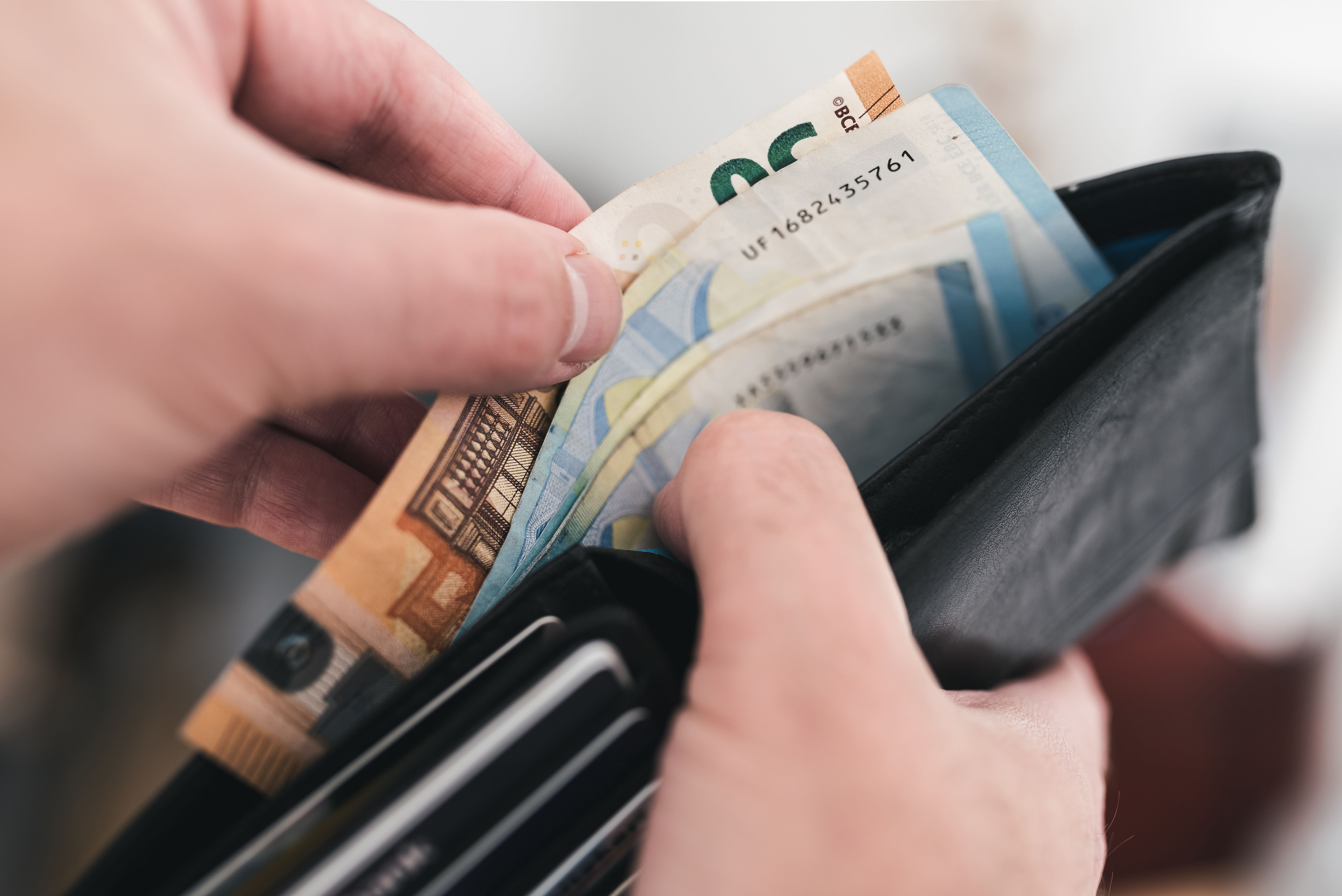 Nahaufnahme von Händen, die Geldscheine aus einem schwarzen Portemonnaie nehmen.