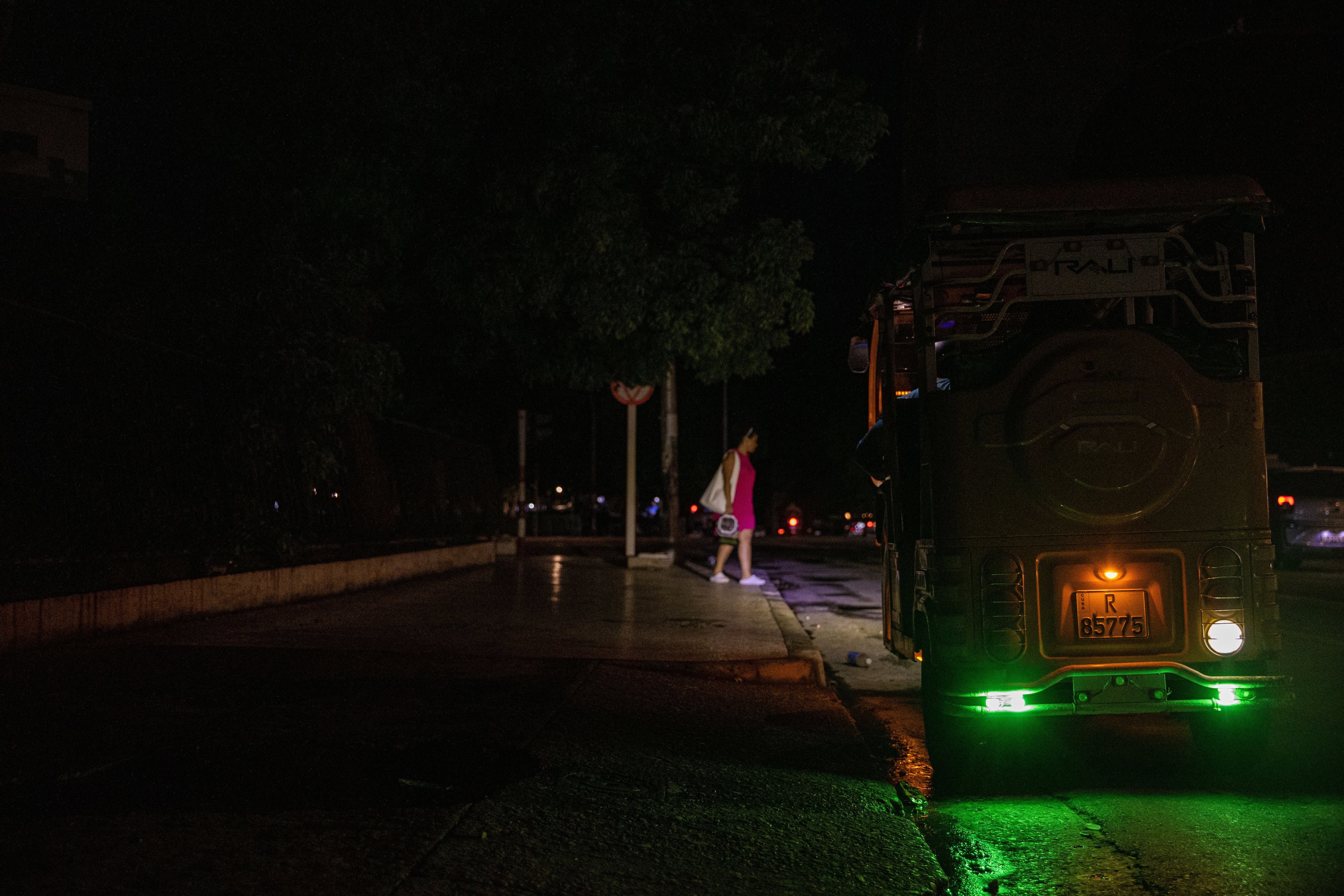 Ein Tuk-Tuk mit grünem Licht steht nachts auf einer dunklen Straße in Havanna.