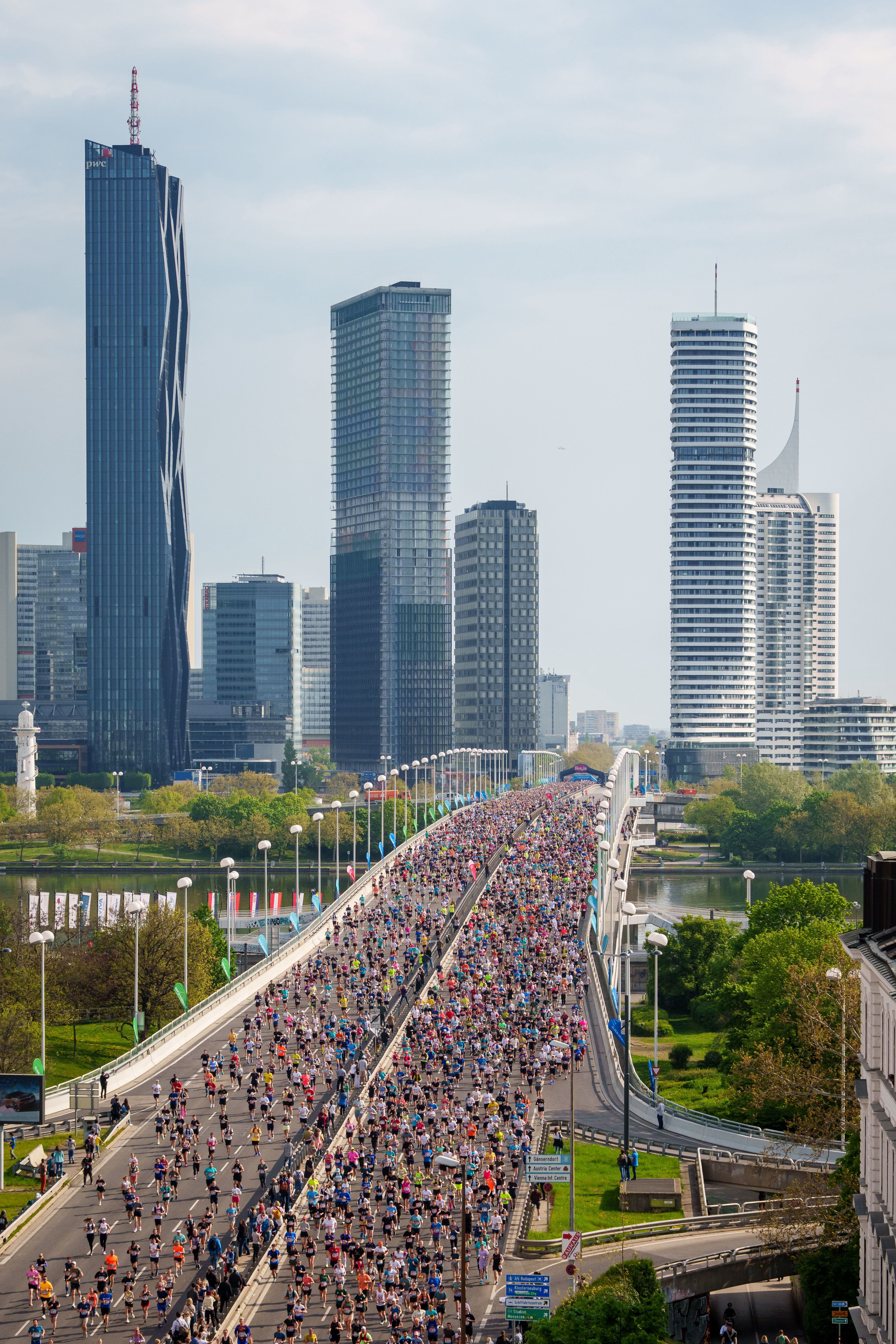 Viele Läufer überqueren bei einem Marathon die Reichsbrücke in Wien vor modernen Hochhäusern.