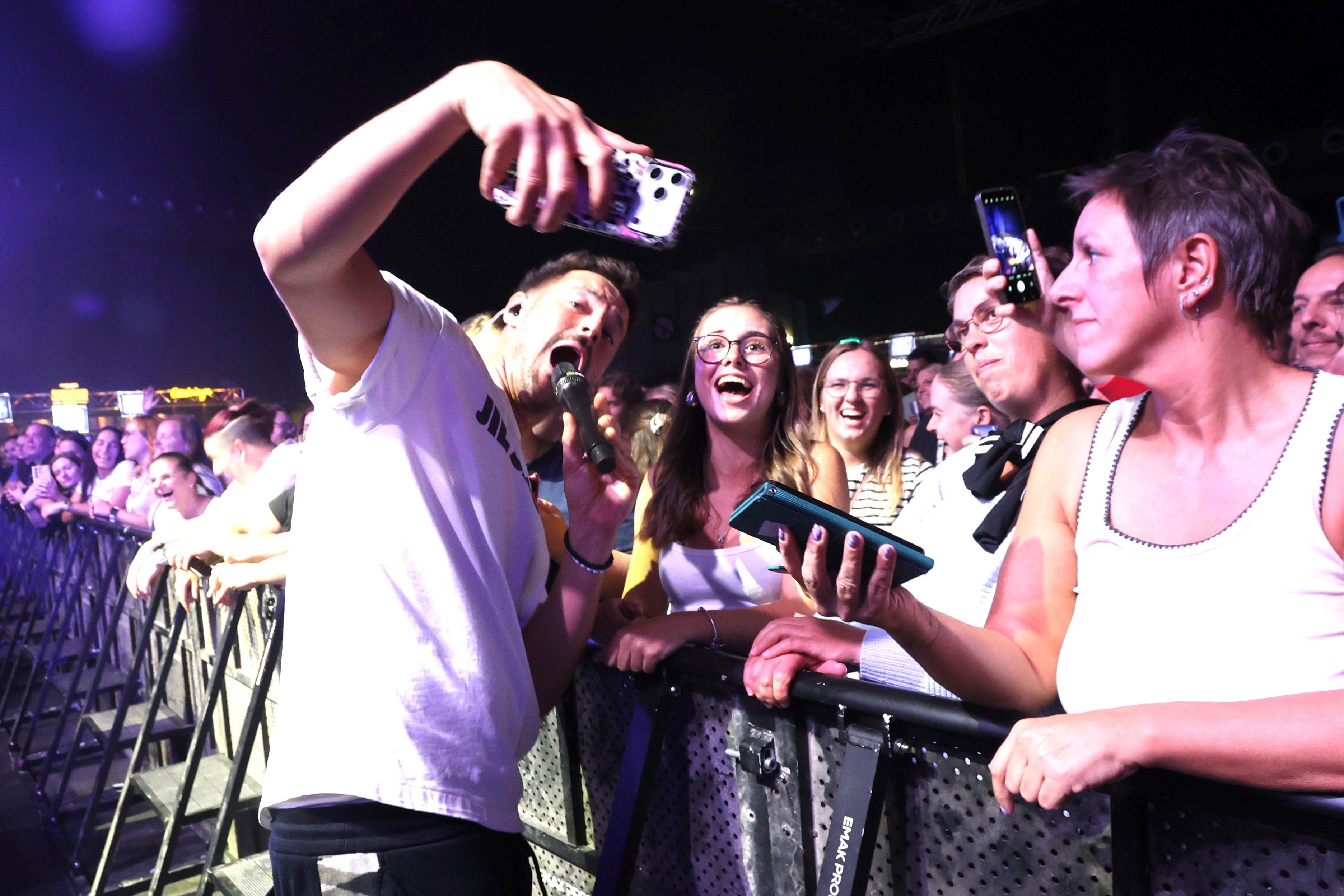 Ein Sänger macht ein Selfie mit jubelnden Fans vor der Bühne bei einem Konzert.